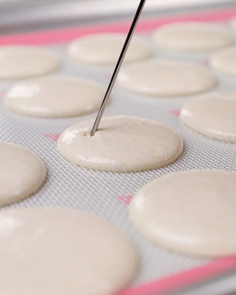 image of white macaron shells that have been piped and banged on the counter, and that are having any small bubbles that surfaced be popped with a scribe