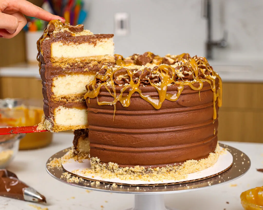 image of a Twix cake that's been cut open to show its fluffy vanilla cake layers, thick caramel filling and shortbread crust