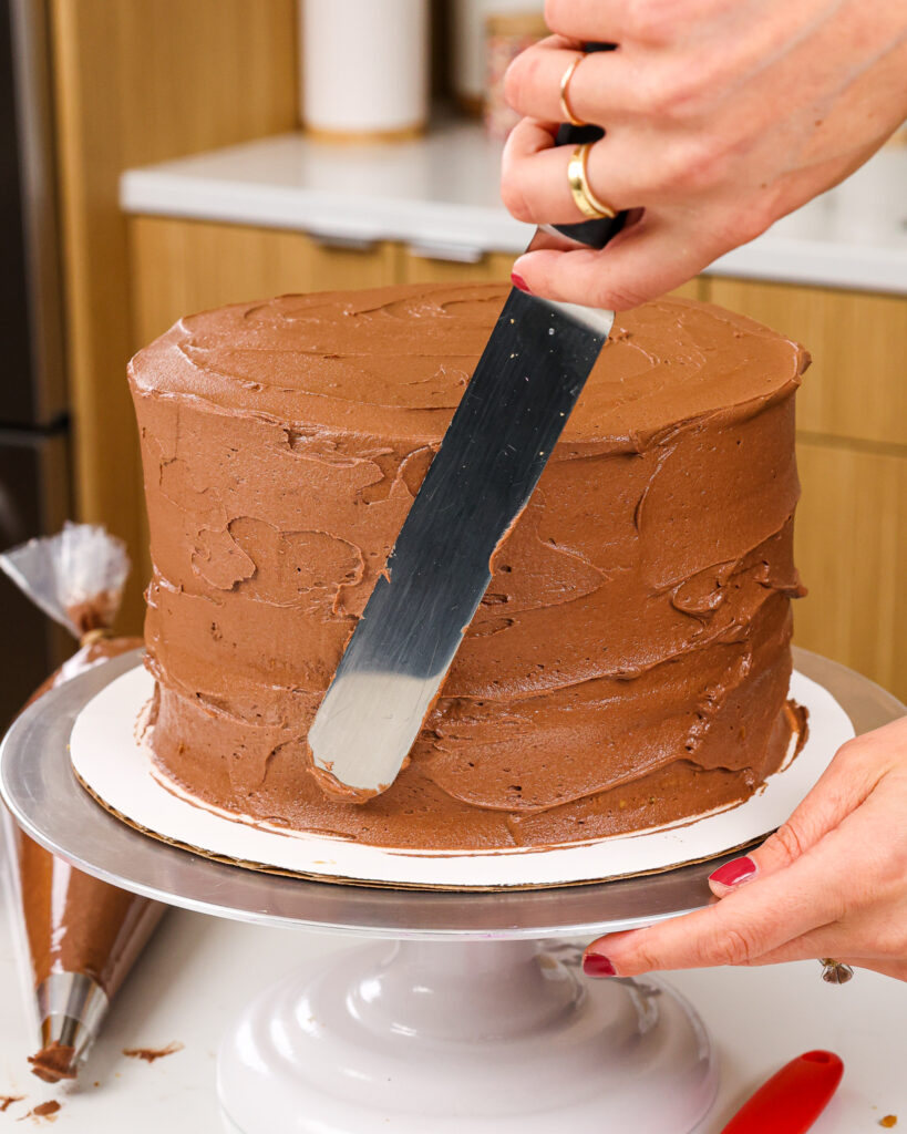 image of a twix cake being crumb coated with a thin layer of semi-sweet chocolate buttercream