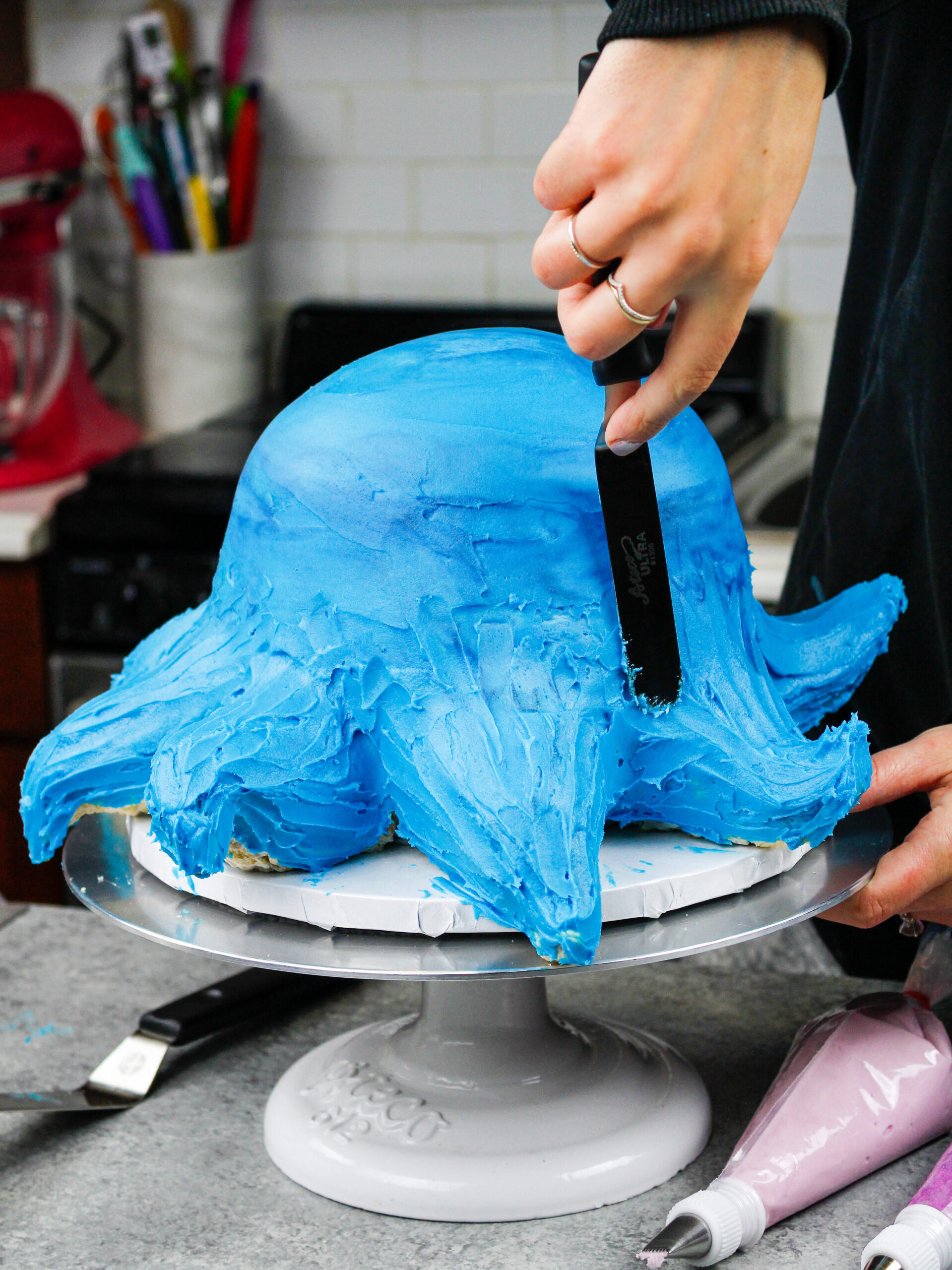 image of an octopus cake being frosted and smoothed using a small offset spatula