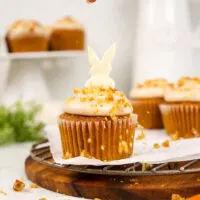 image of a walnut brittle topping being sprinkled over carrot cake cupcakes