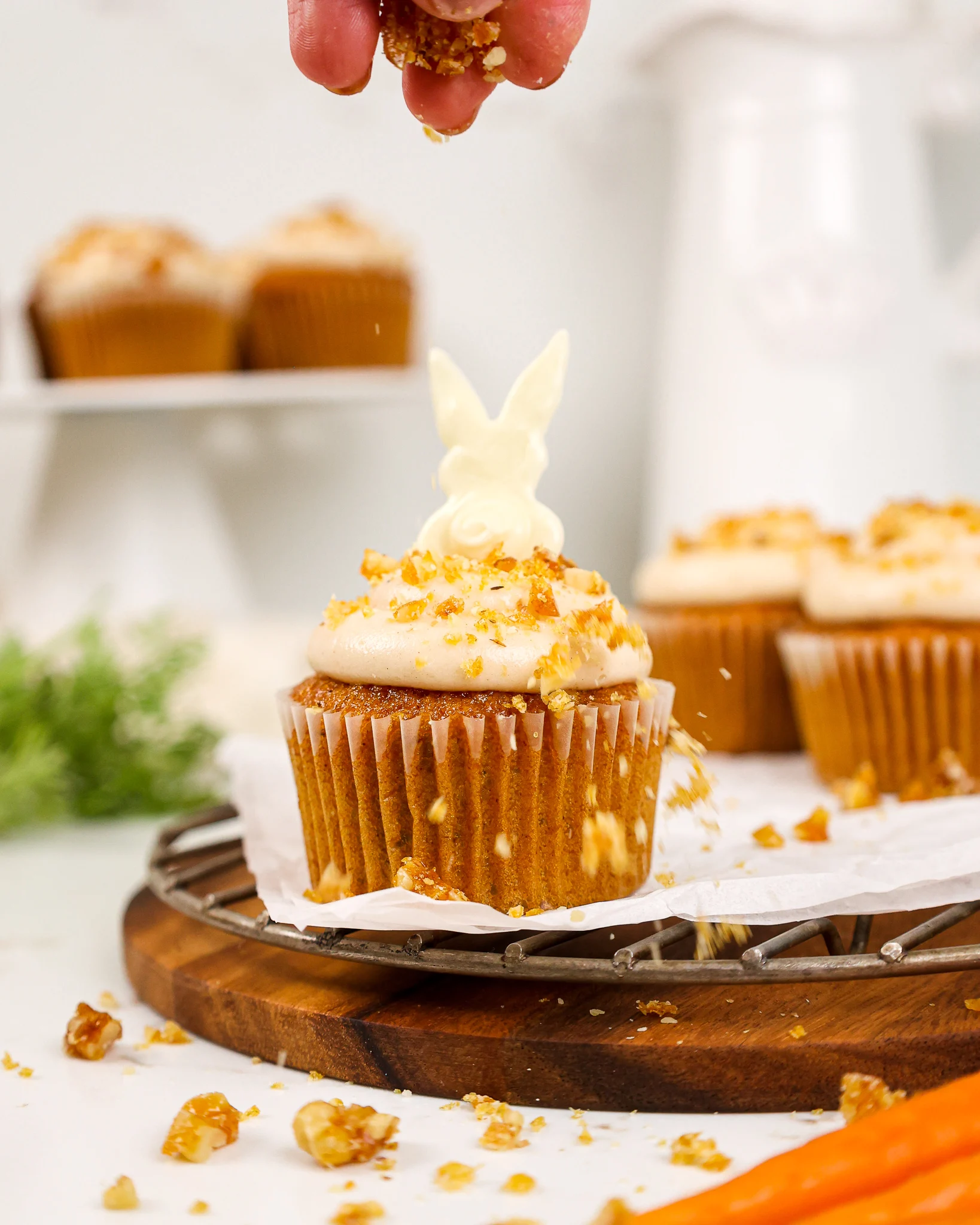image of a walnut brittle topping being sprinkled over carrot cake cupcakes