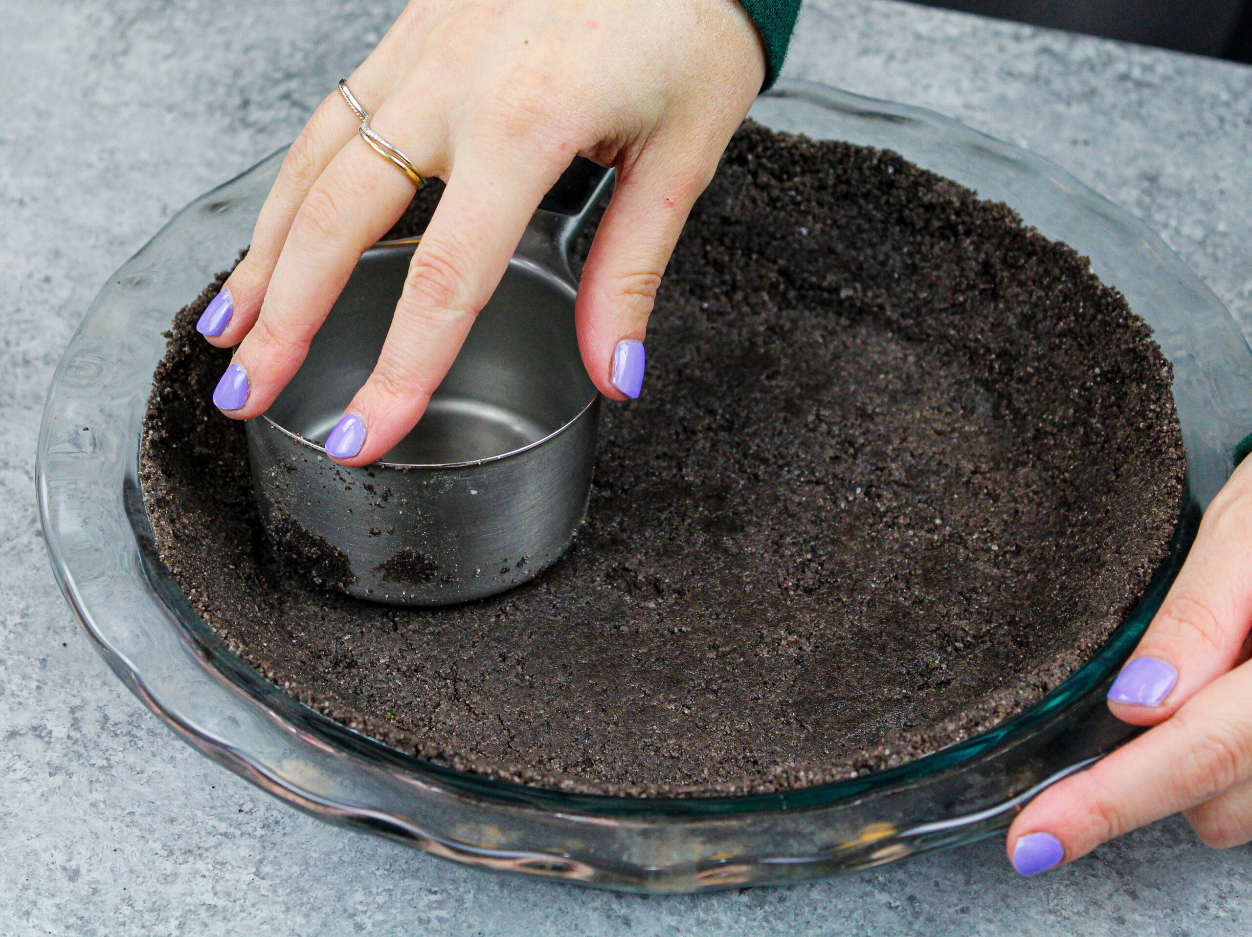 image of an oreo pie crust being made and pressed into a pie pan using a metal measuring cup