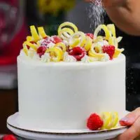 image of lemon raspberry layer cake being dusted with powdered sugar