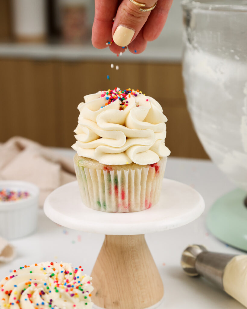 image of sprinkles being added to a cupcake frosted with a perfectly sweet buttercream