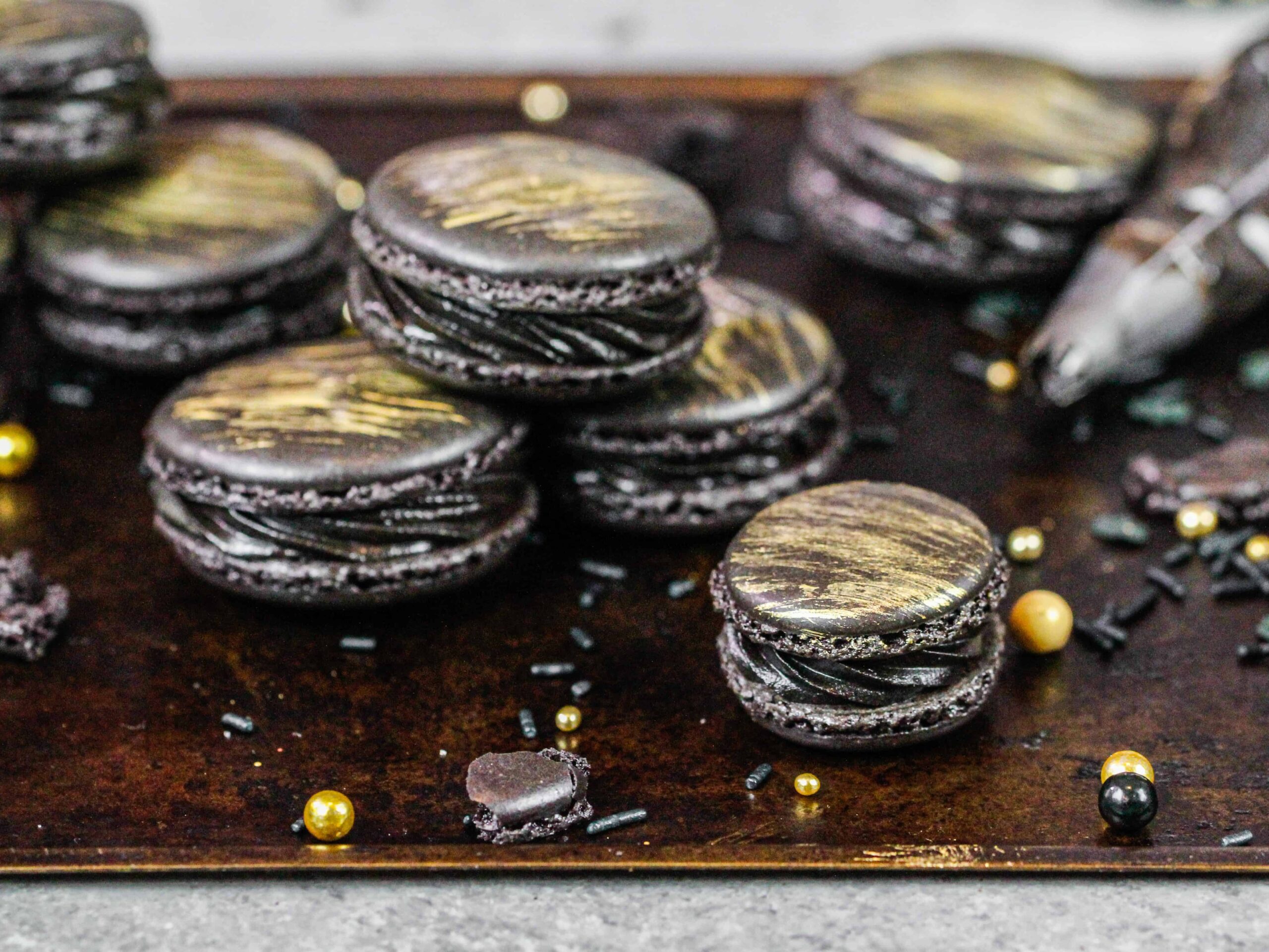 image of french black macarons that have been filled with black frosting and brushed with a beautiful gold streak of edible gold paint