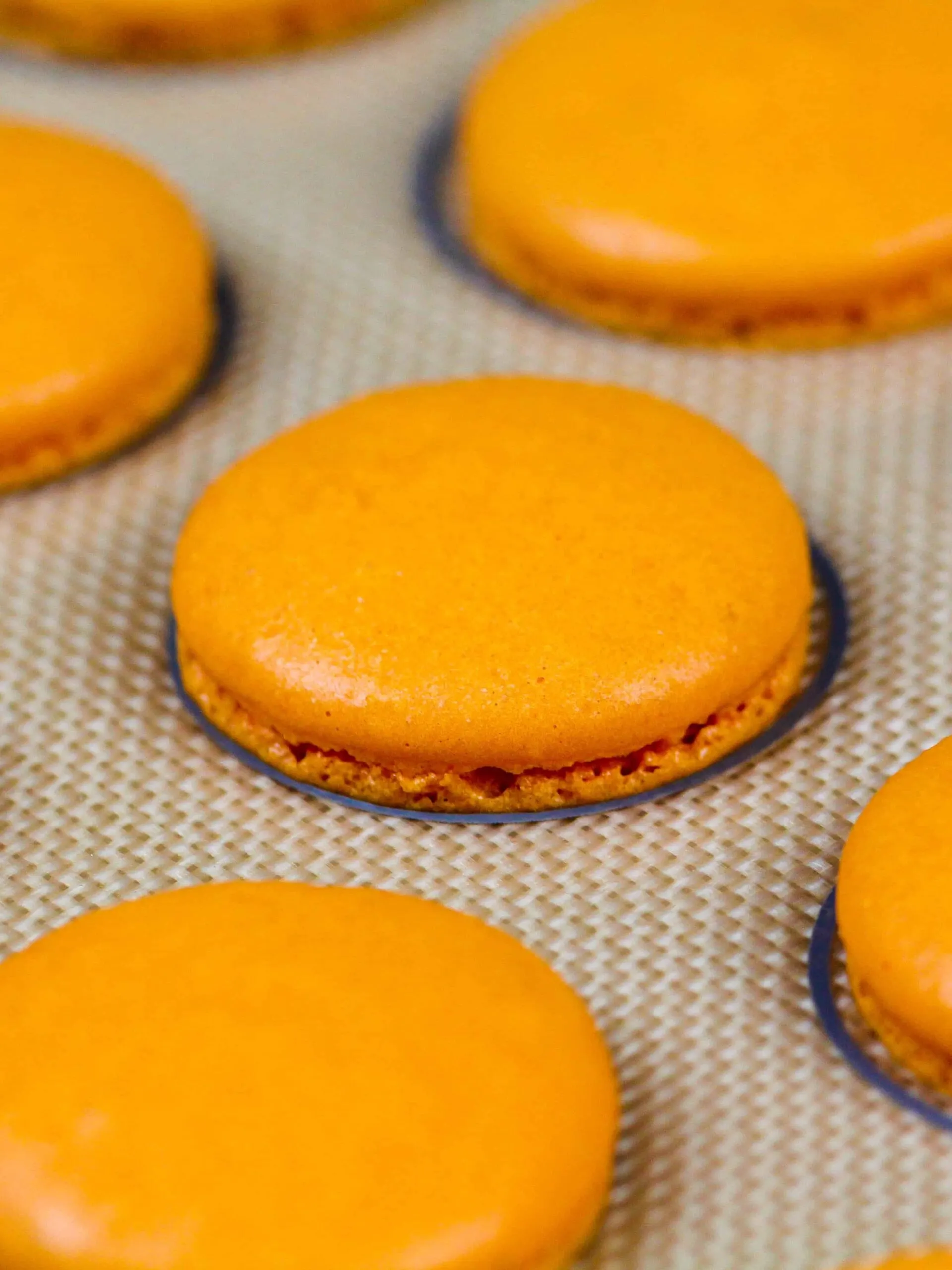 image of orange macaron shells baked on a silpat mat and cooling