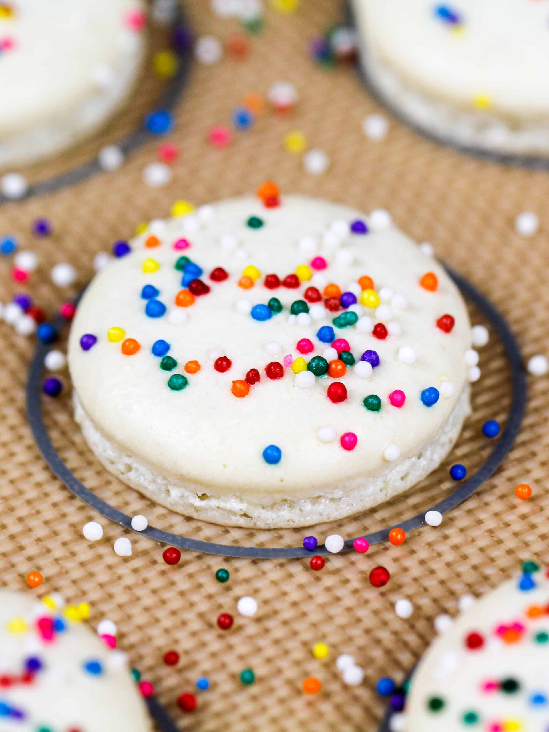 image of baked white macaron shells topped with nonpareil sprinkles to make rainbow macarons