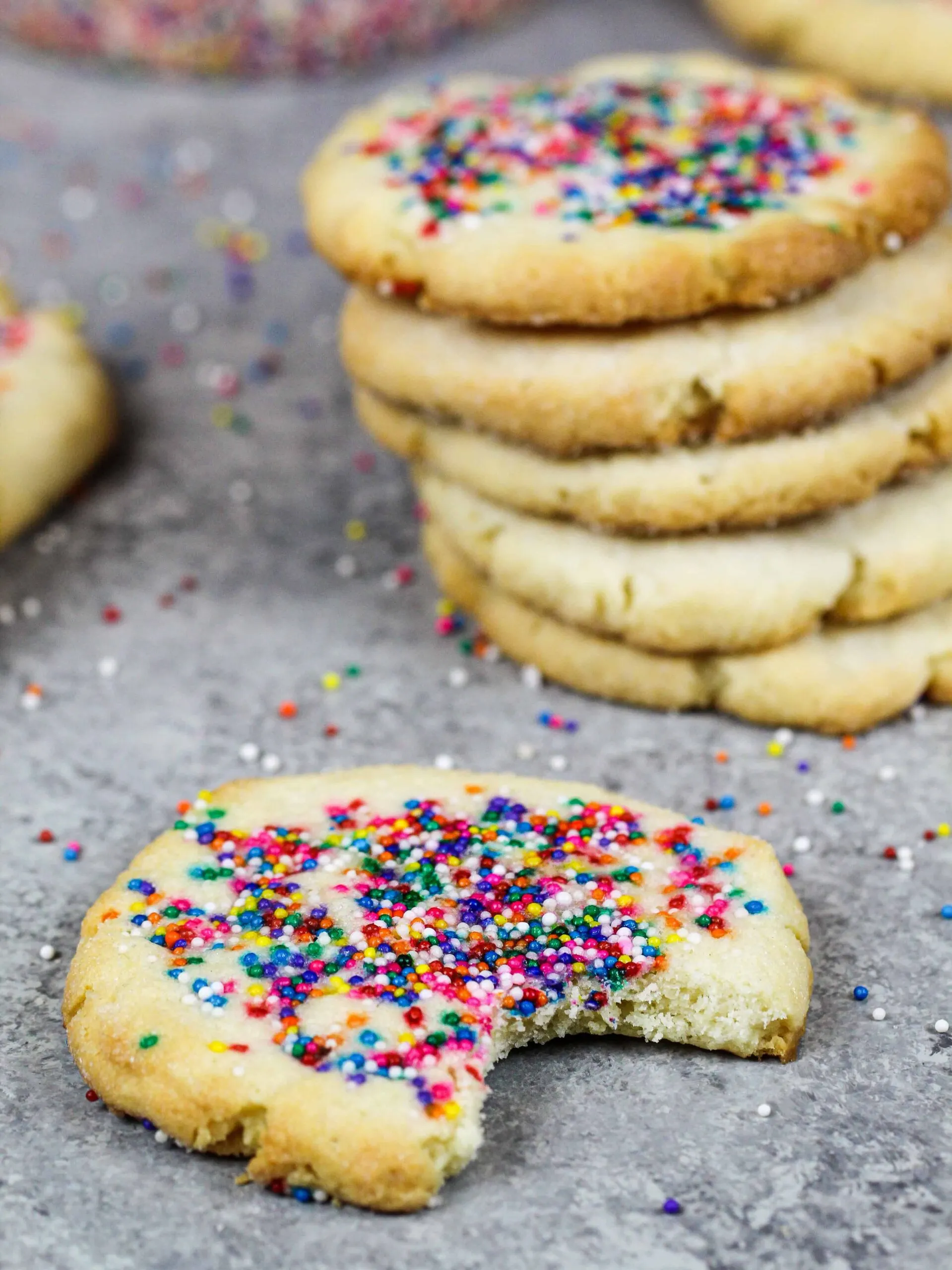 image of cream cheese shortbread cookies topped with nonpareil sprinkles that's been bitten into to show it's tender texture