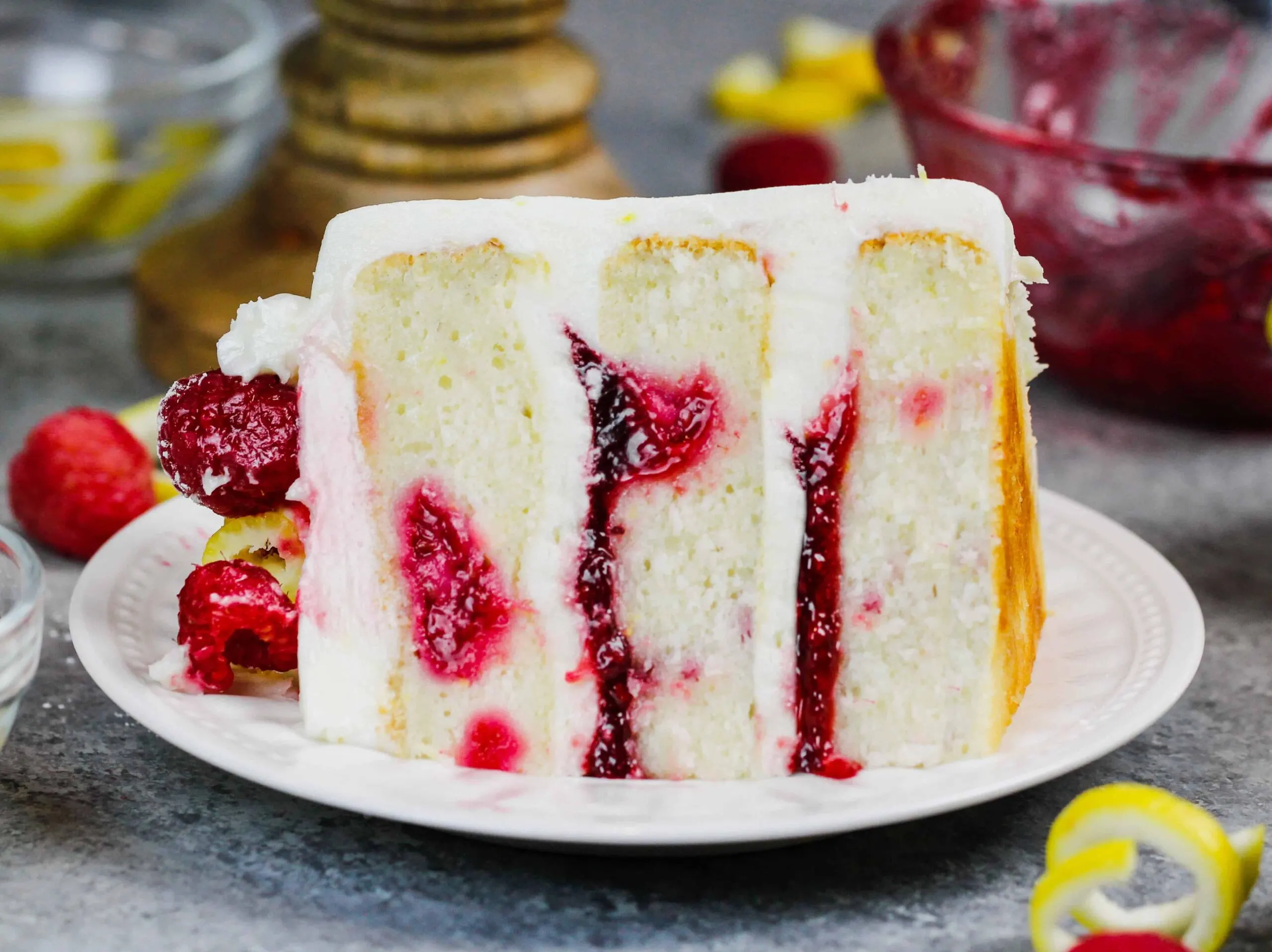 image of a slice of lemon rapsberry cake on a plate, showing it's raspberry filling and lemon cream cheese frosting
