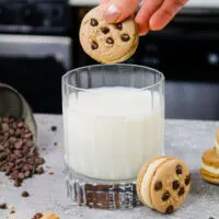 image of cookie dough macarons filled with cookie dough buttercream being dunked into a glass of milk