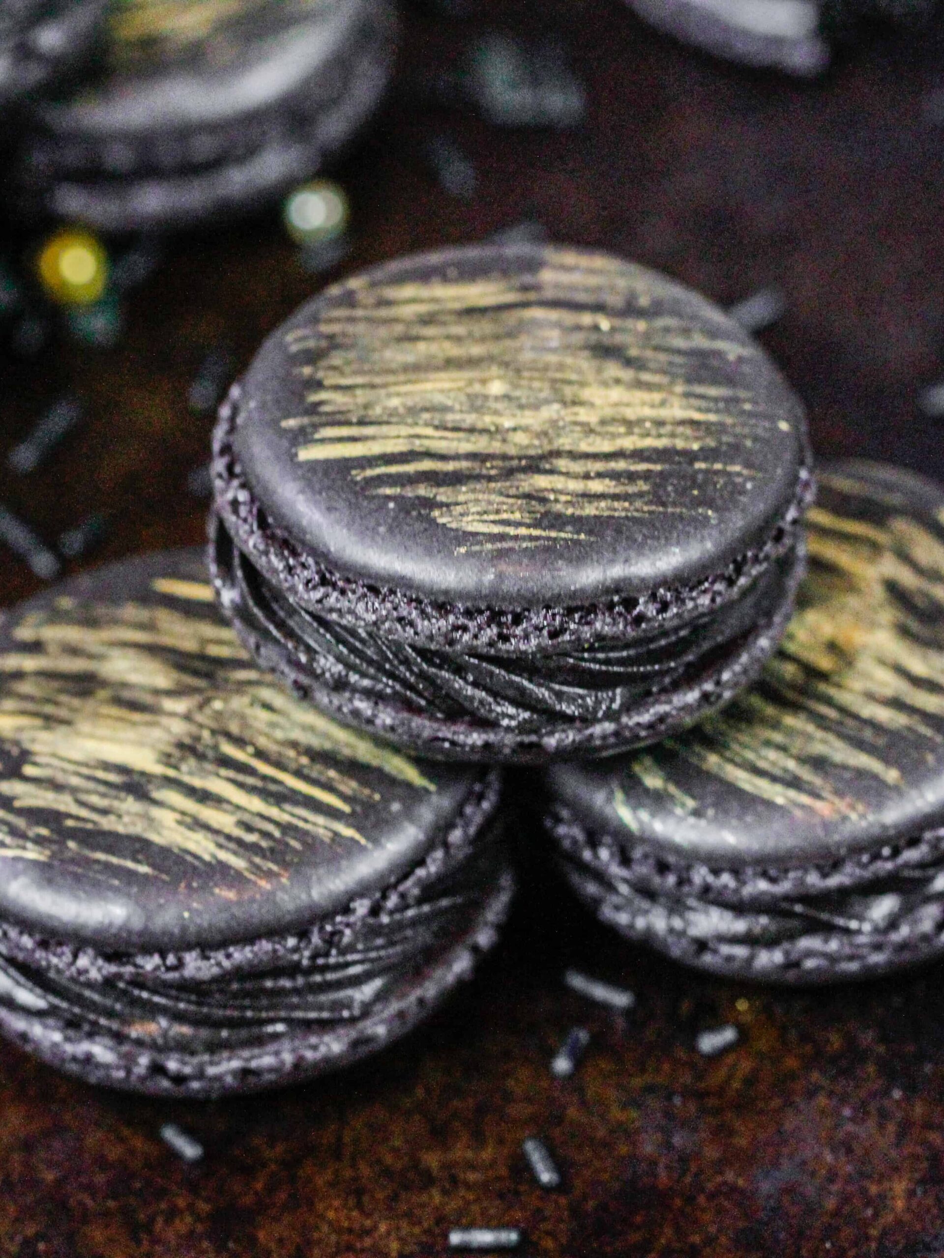 image of french black macarons that have been filled with black frosting and brushed with a beautiful gold streak of edible gold paint