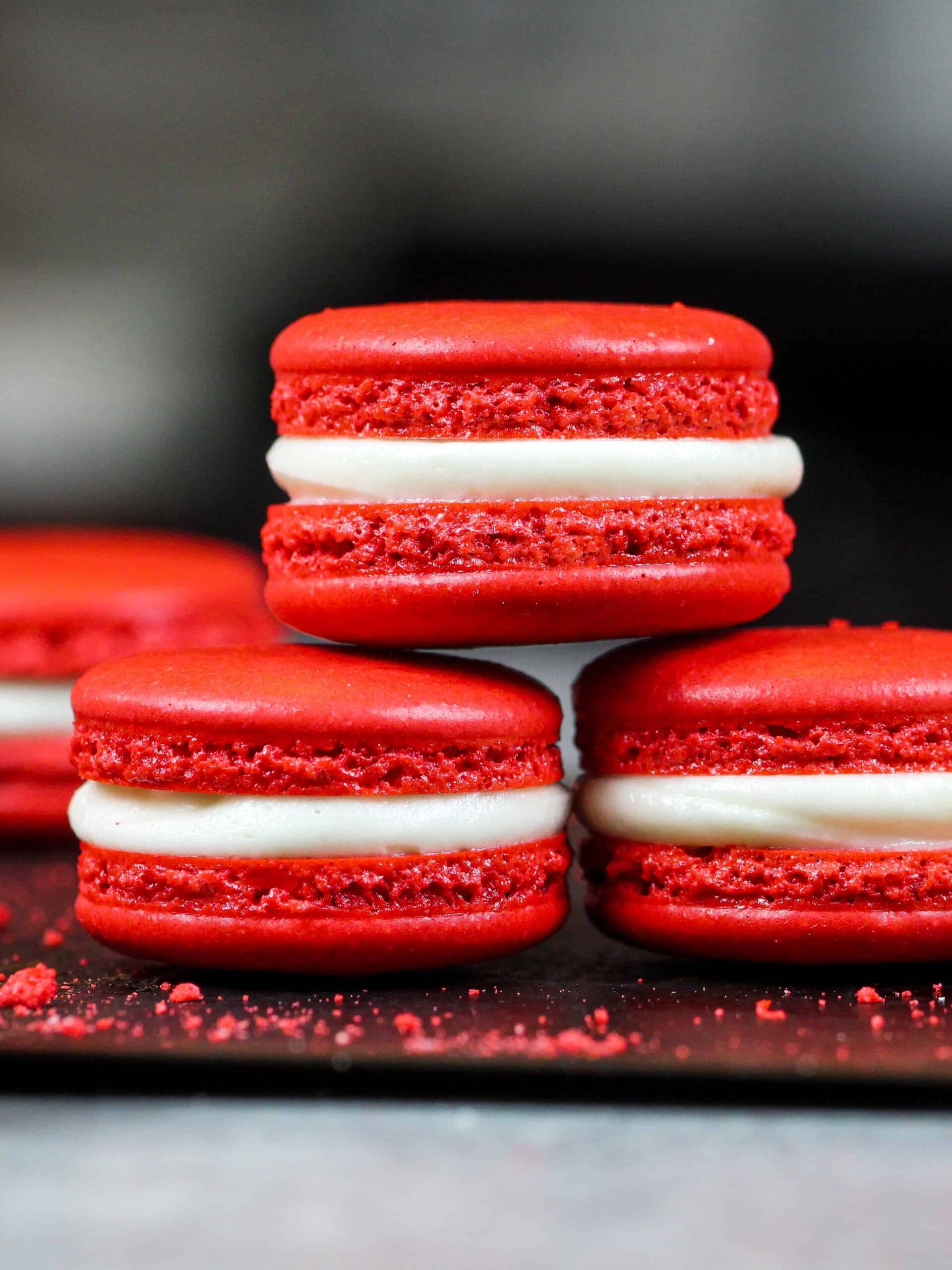 image of red velvet macarons filled with cream cheese frosting that are stacked on each other to show their perfect feet