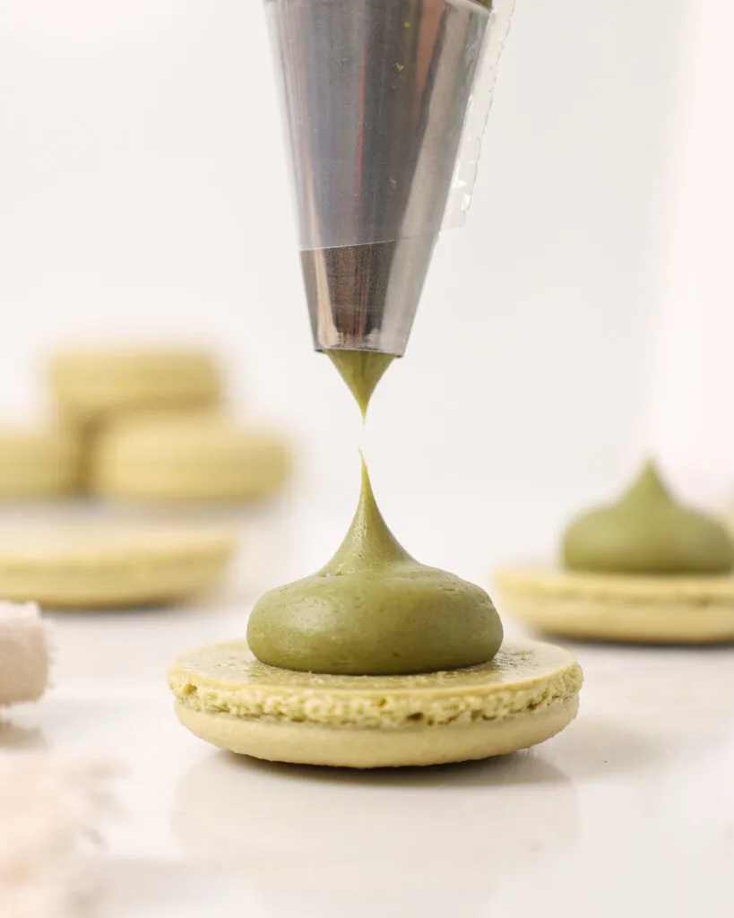image of matcha ganache being piped on to a matcha macaron shells