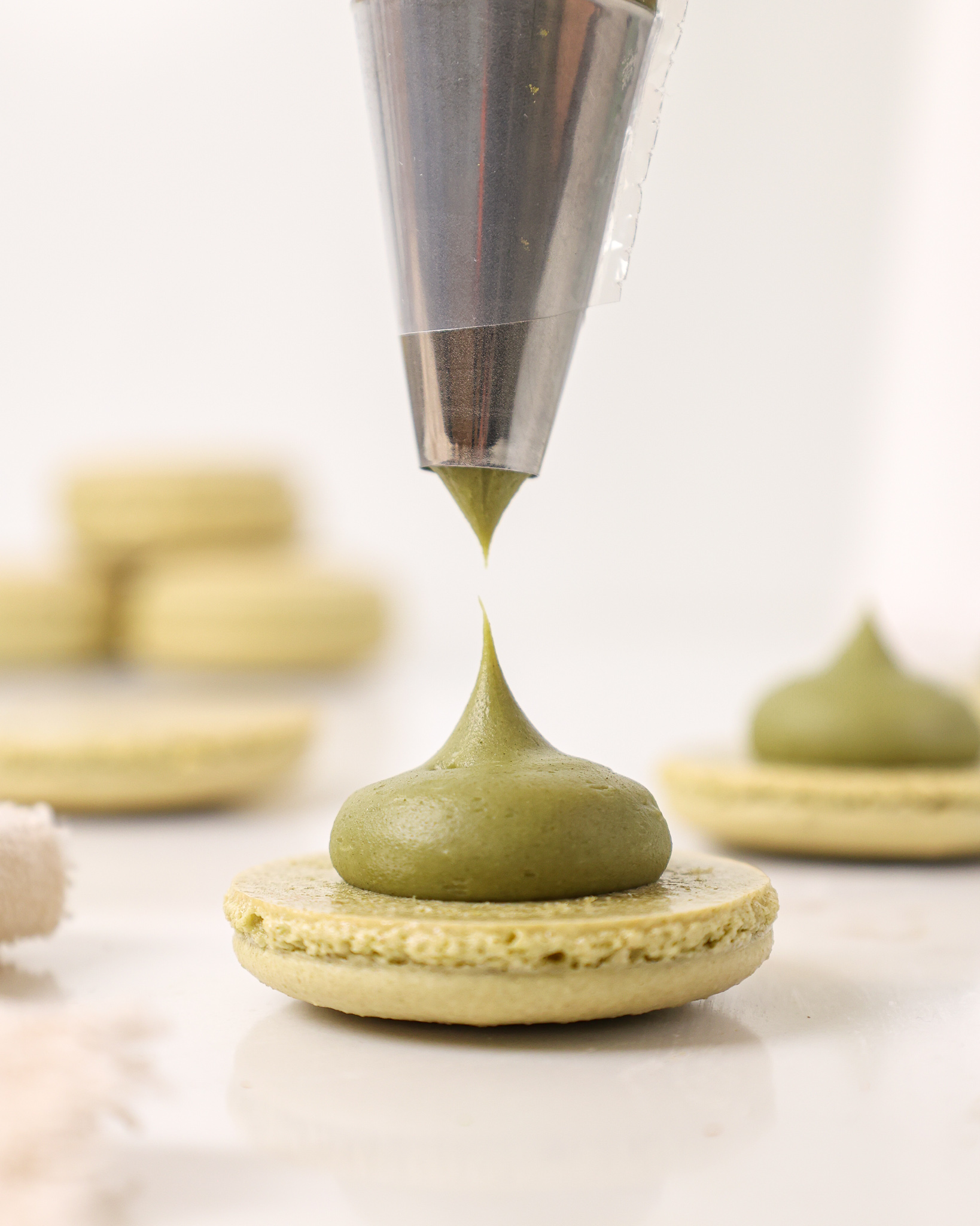 image of matcha ganache being piped on to a matcha macaron shells