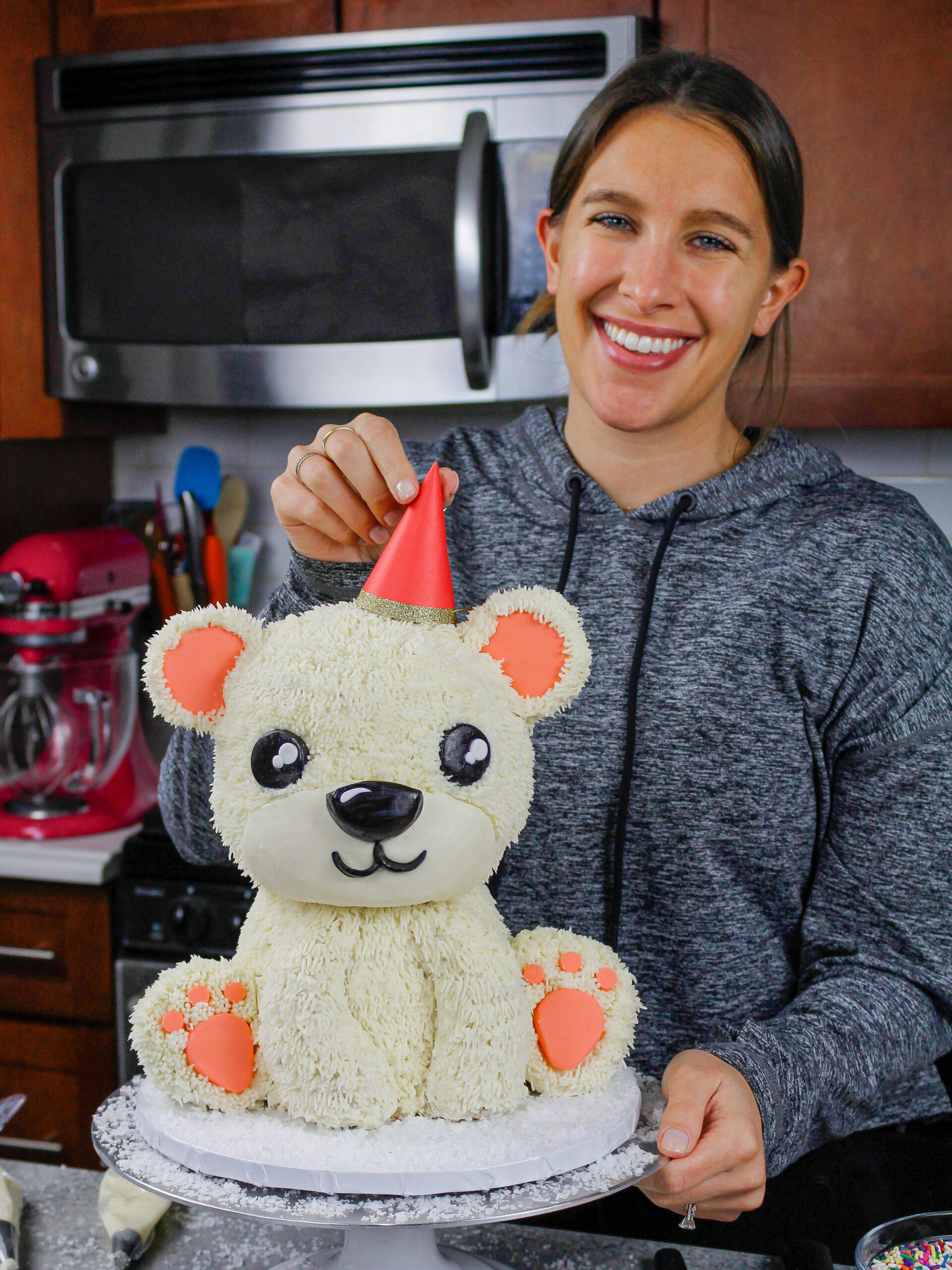 image of chelsey white of chelsweets putting a party hat on her polar bear cake, which was made as part of her animal cake series