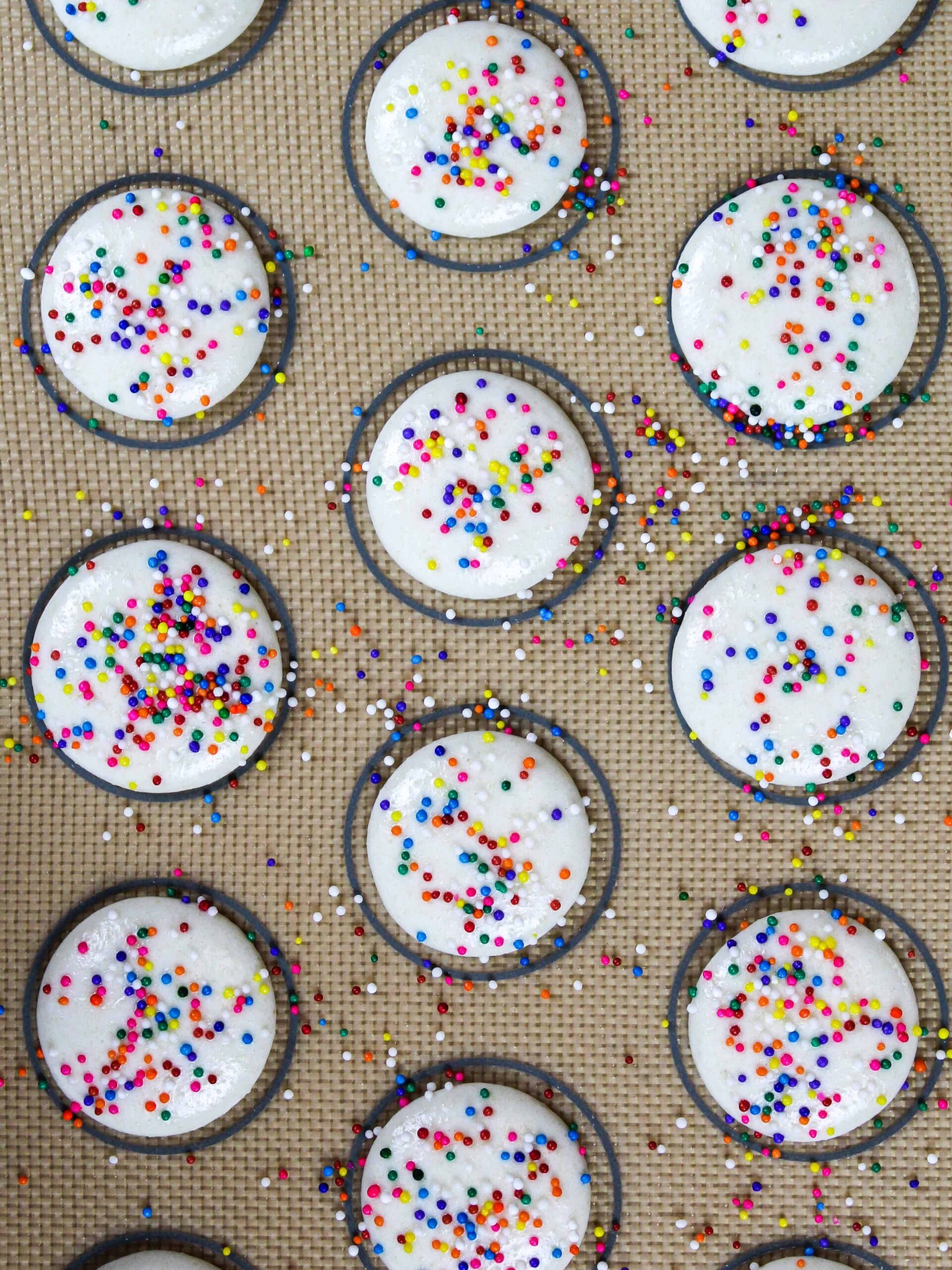 image of white macaron shells topped with rainbow sprinkles being rested before being baked