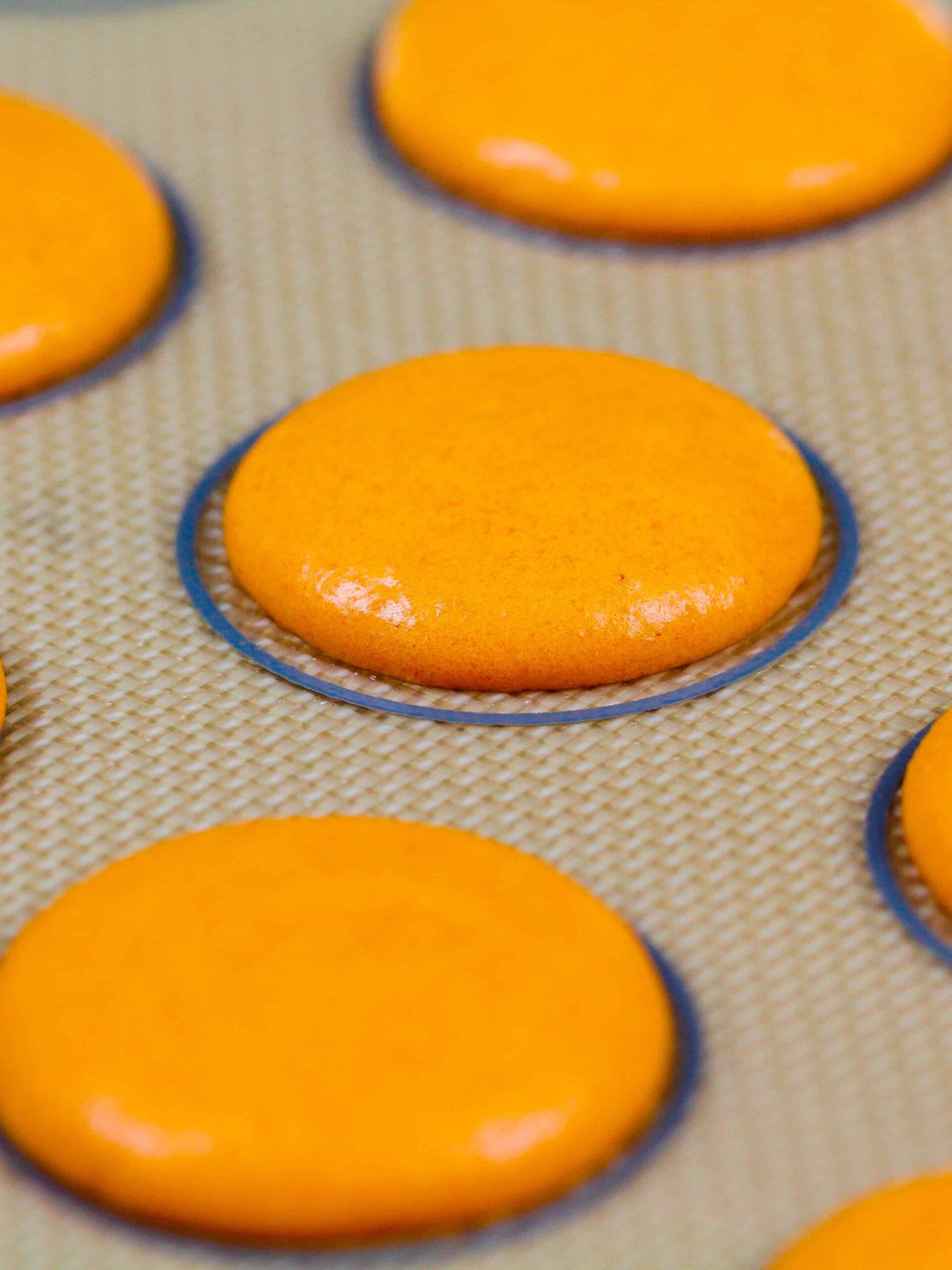image of orange french macaron batter being piped onto a silpat mat to make pumpkin macarons