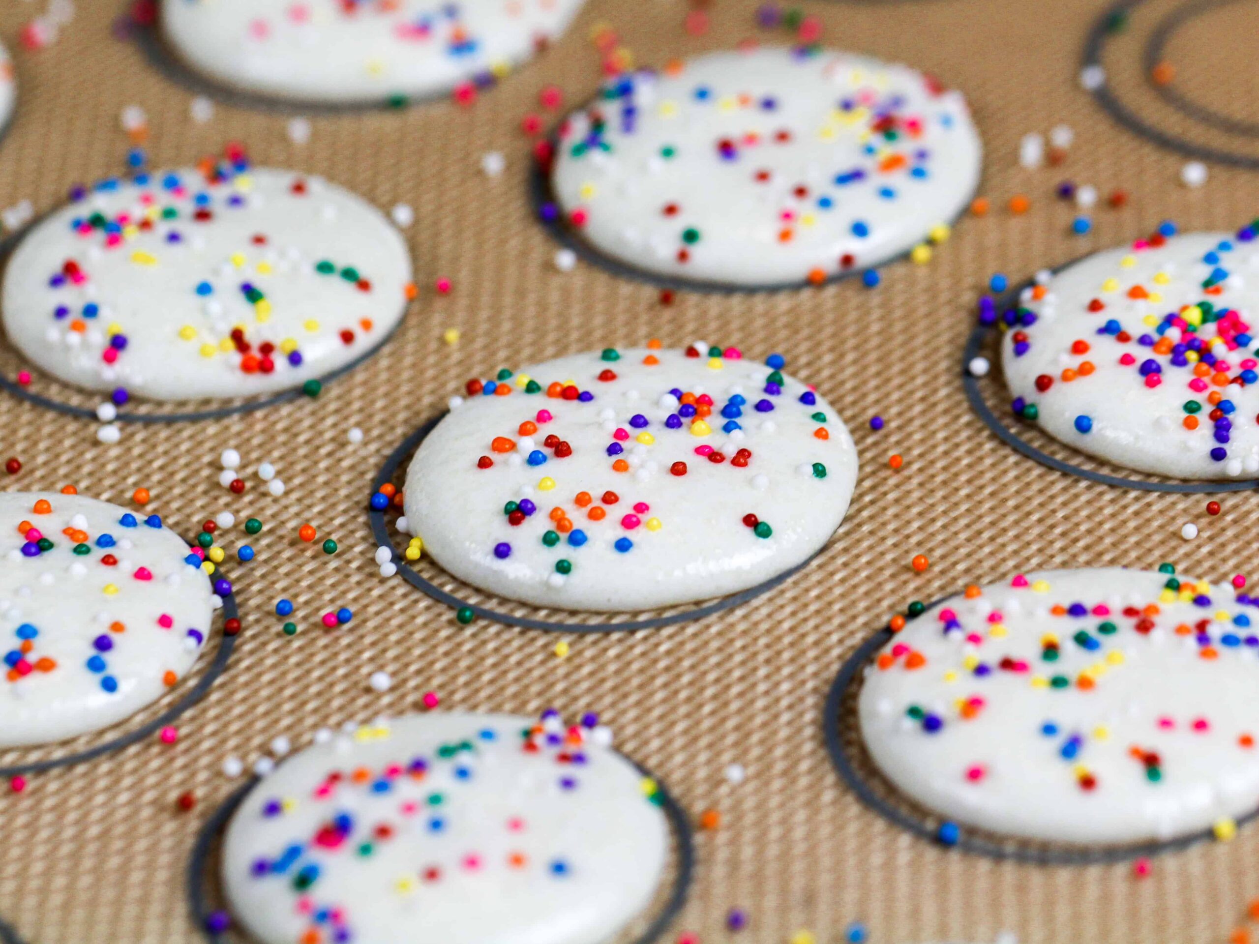 image of white macaron shells topped with rainbow sprinkles that have rested and are ready to be baked