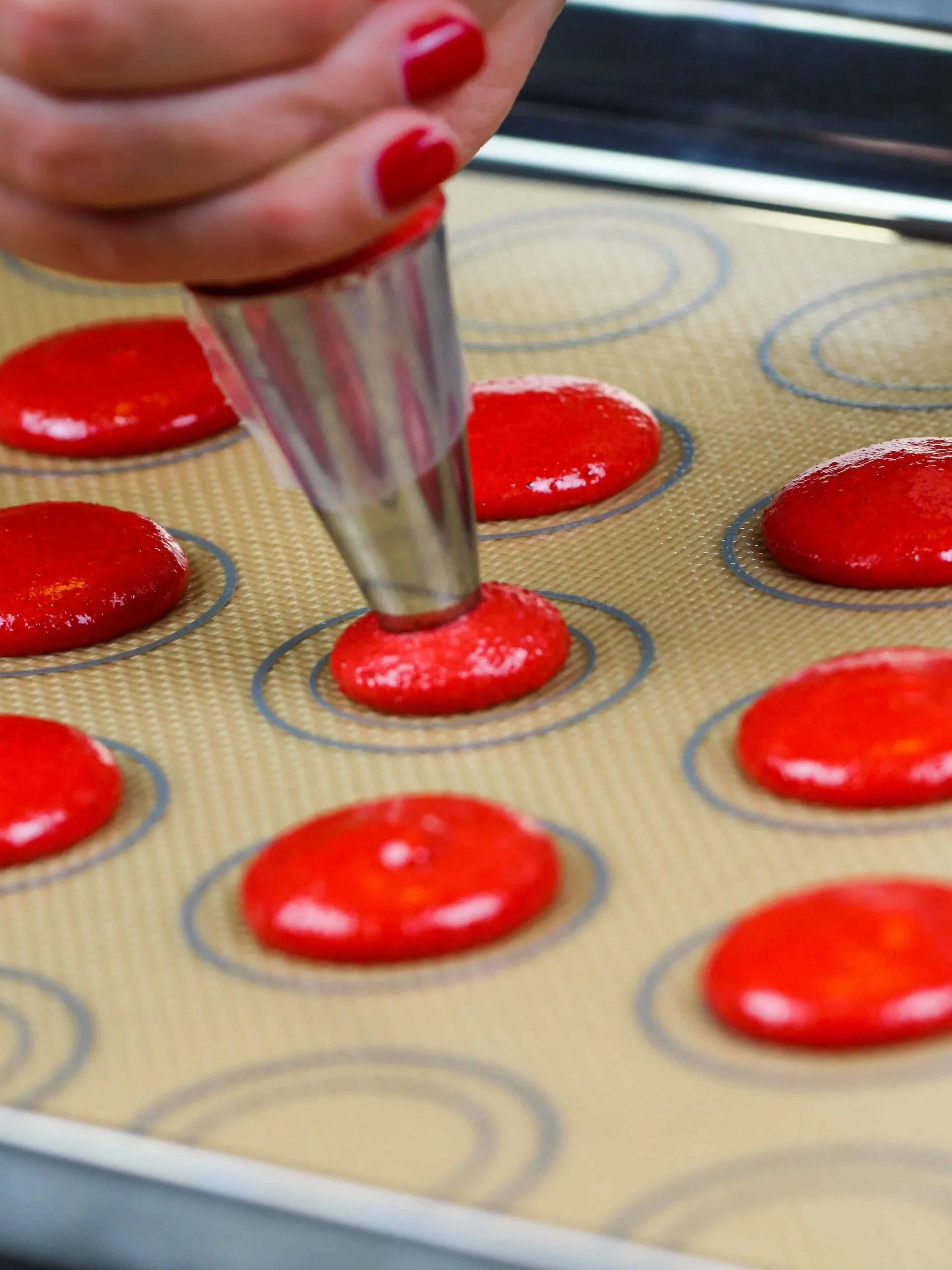 image of french red velvet macaron batter being piped onto a silpat mat