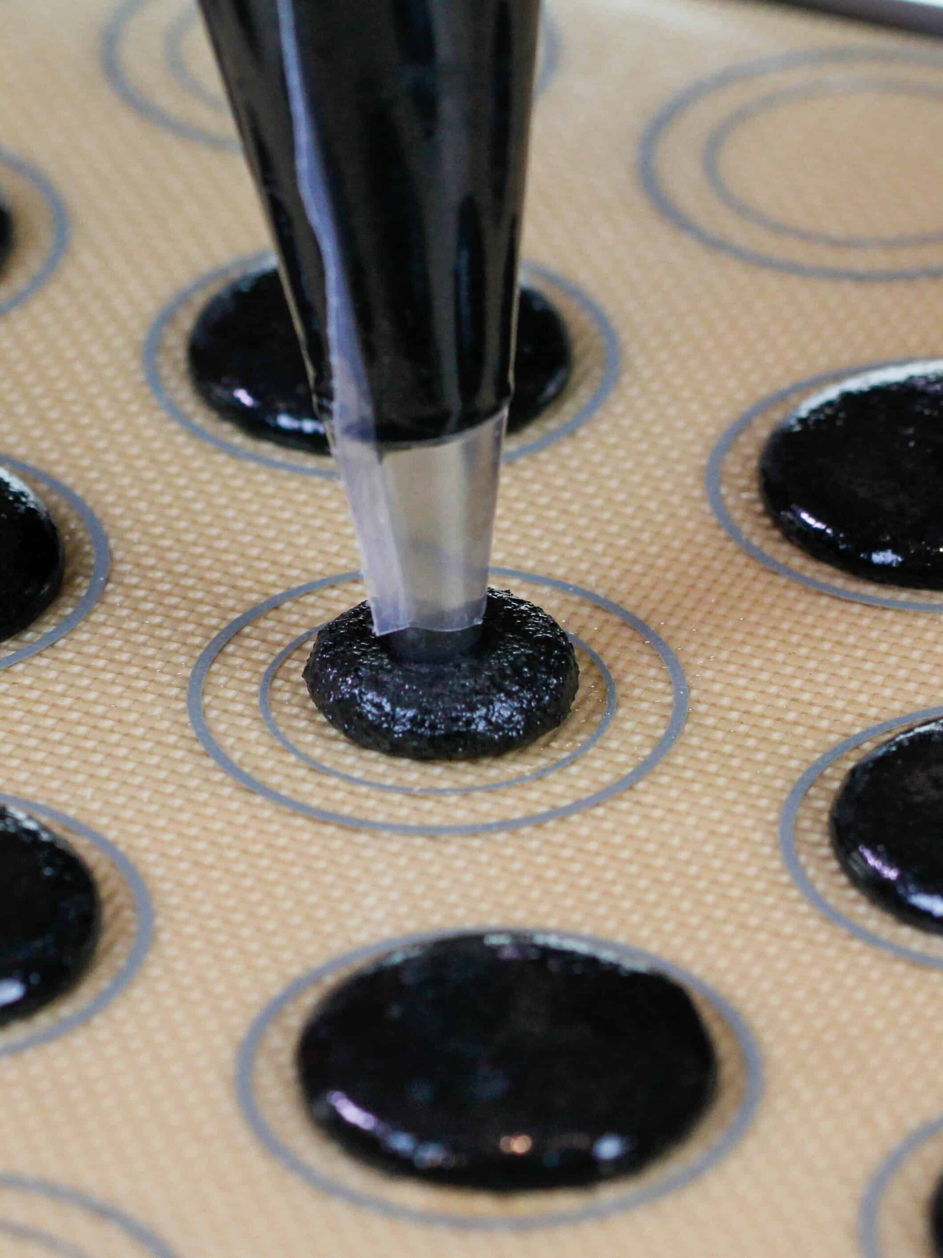 image of black chocolate macarons being piped onto a silpat mat