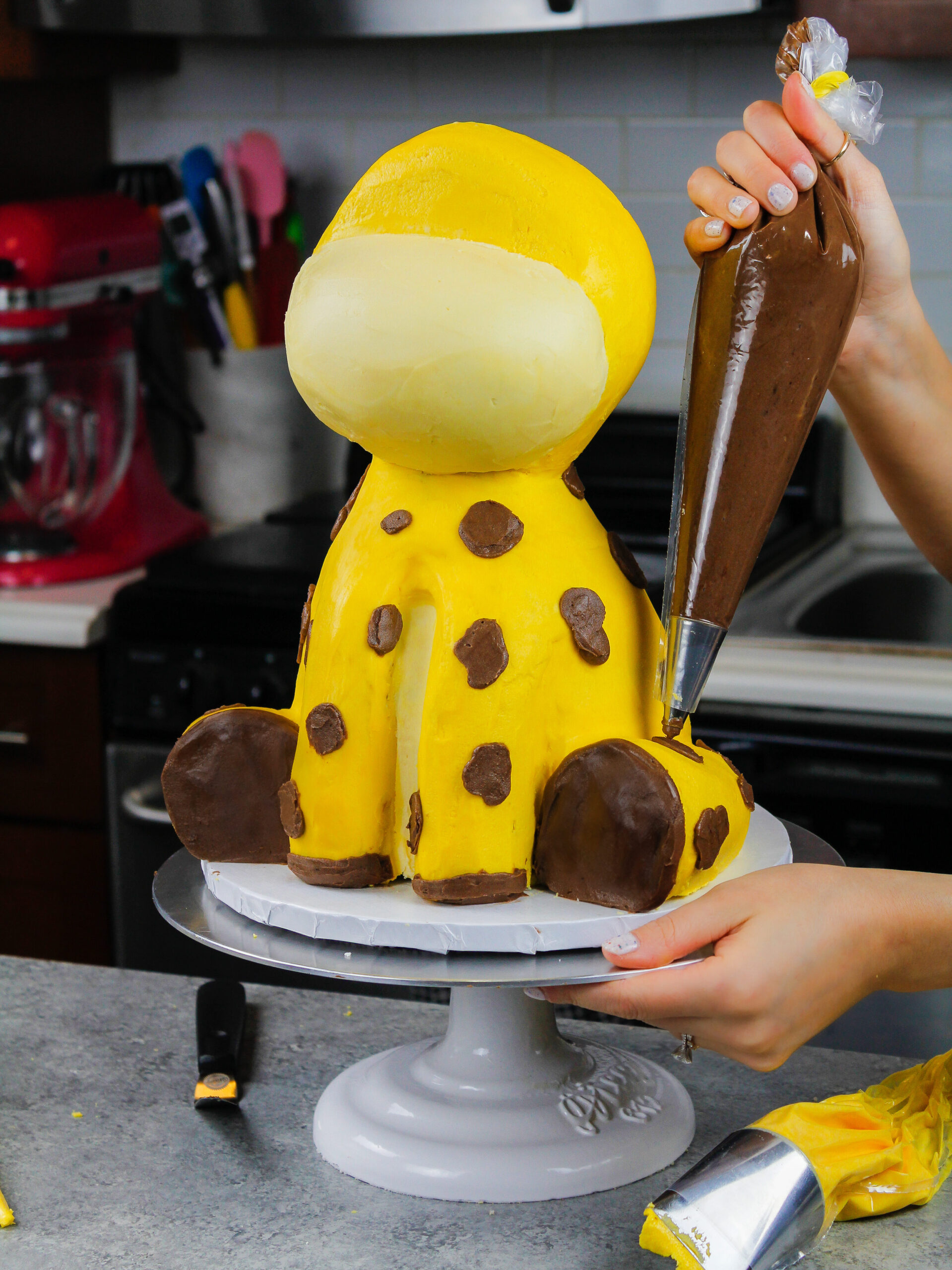 image of a giraffe cake that is having its spots piped on using chocolate buttercream