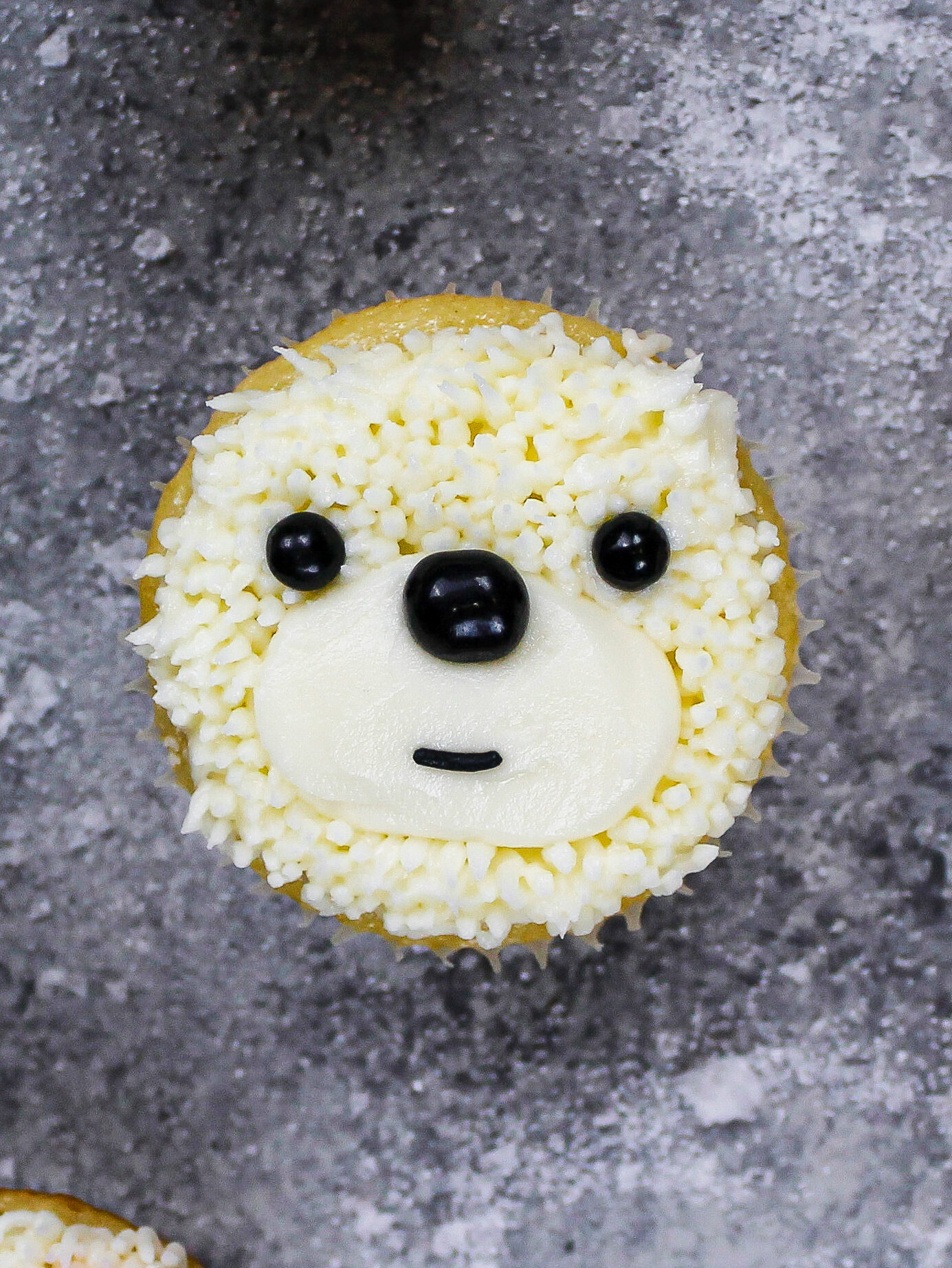 image of a polar bear cupcake being made with buttercream and black sprinkles for the face