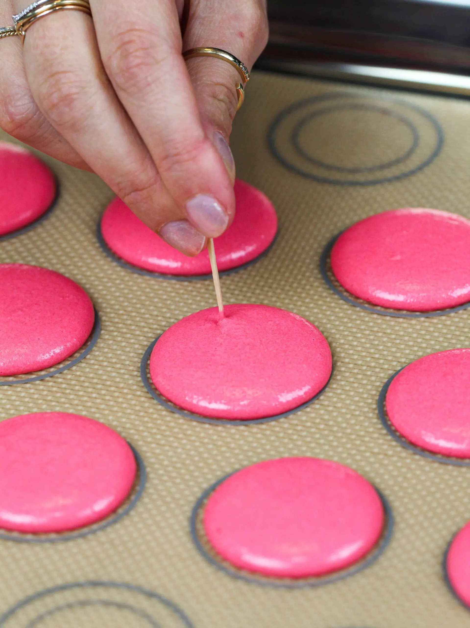 image of pink macaron shells that've been piped and are having their air bubbles popped with a toothpick