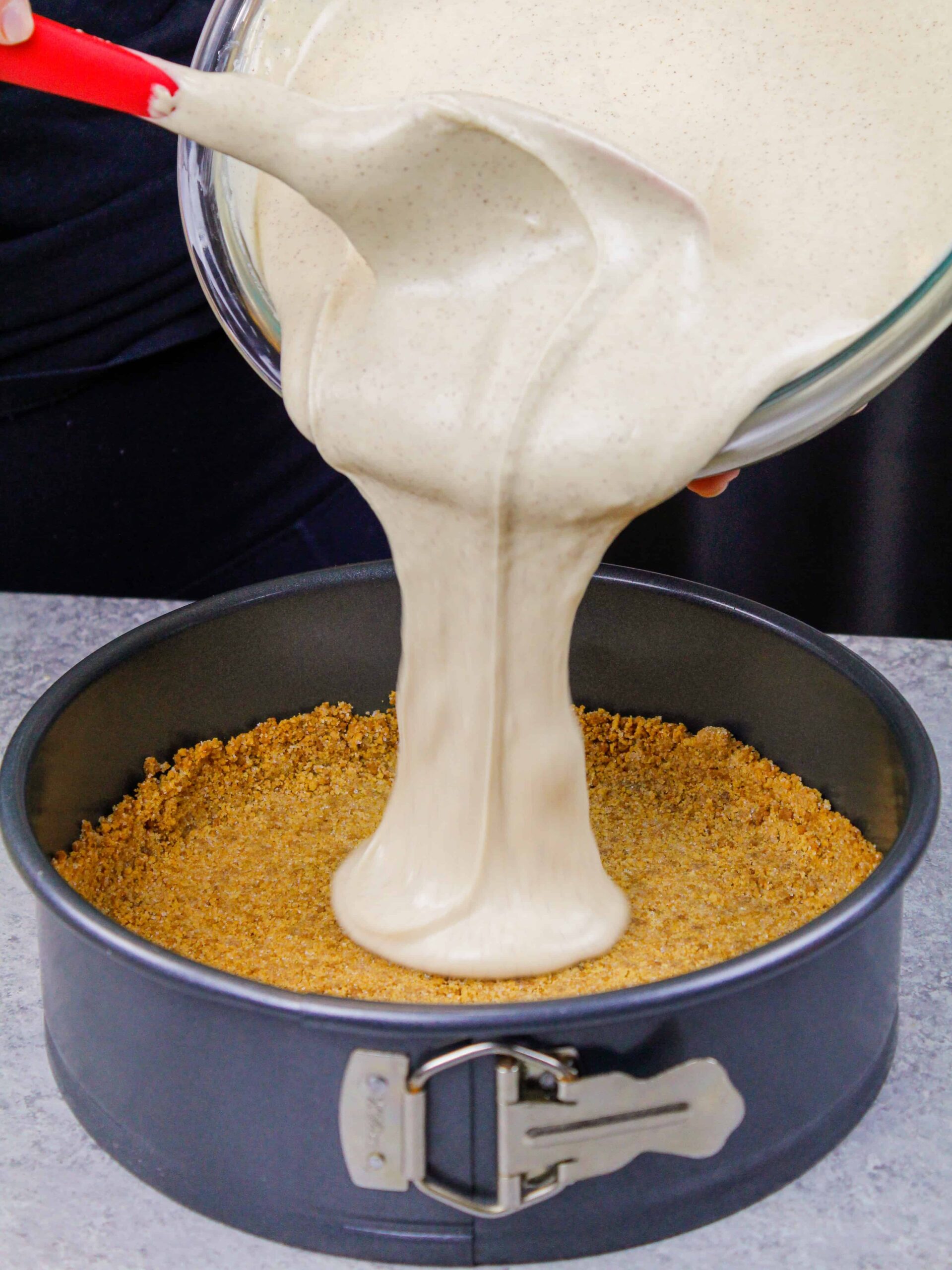 image of cinnamon cookie butter cheesecake batter being poured onto a biscoff cookie crust to make a cheesecake