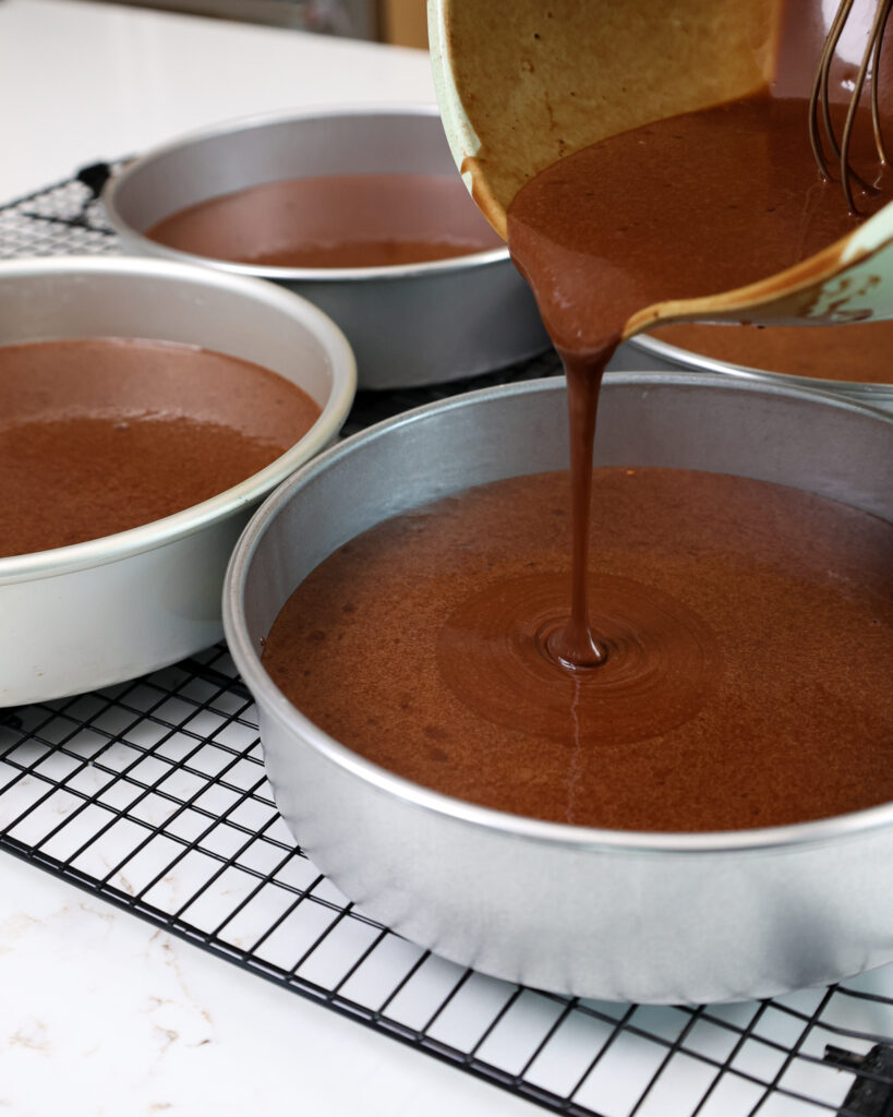 image of chocolate cake batter being poured into 8-inch cake pans