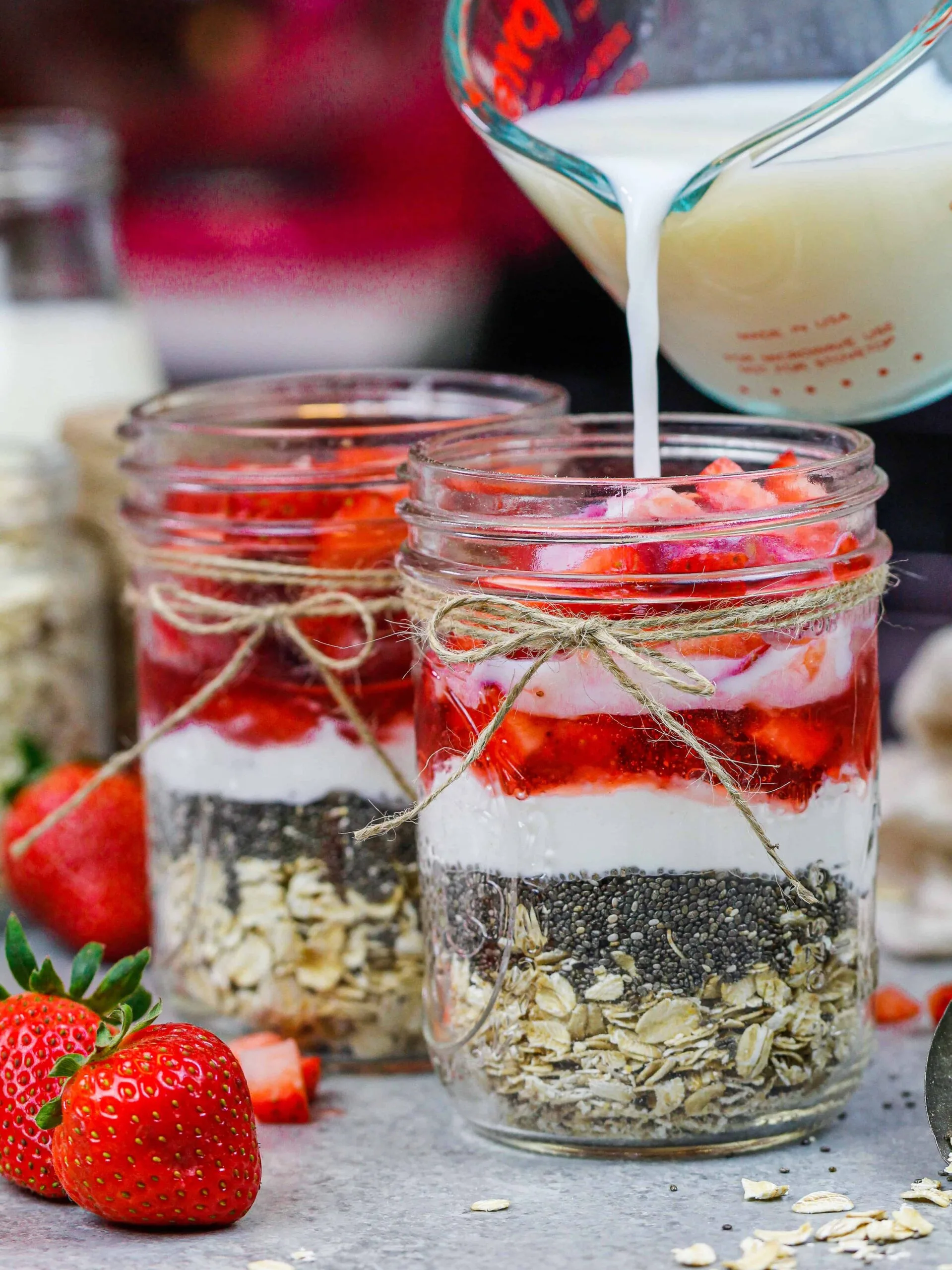 image of milk being poured into a mason jar filled with ingredients to make strawberry overnight oats