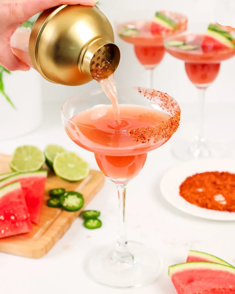 image of a watermelon jalapeno margarita being poured into a tajin rimmed margarita glass