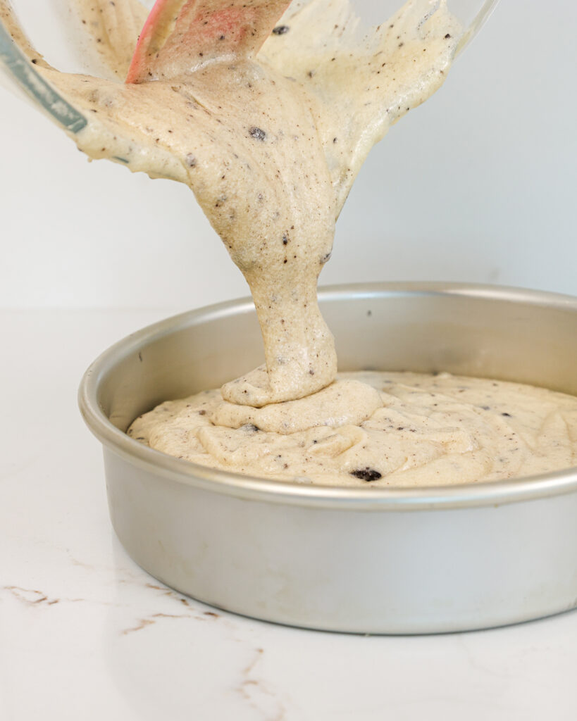 image of vanilla oreo cake batter being poured into an 8-inch cake pan