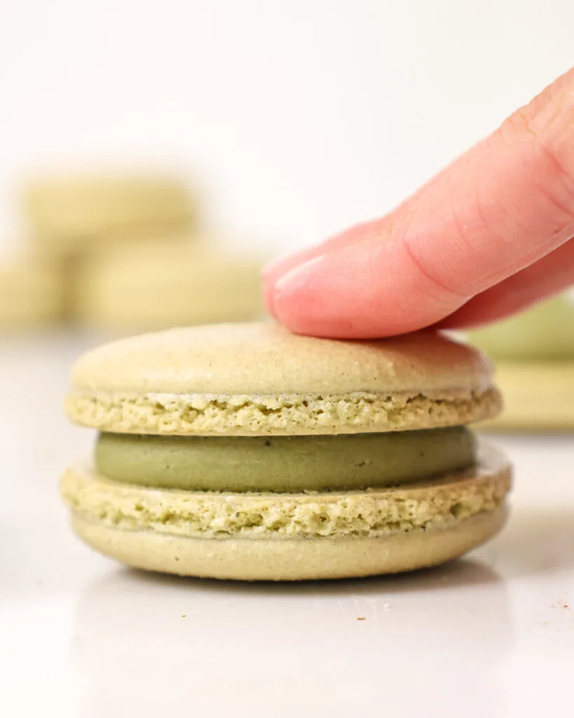 image of a matcha macaron being filled with matcha ganache and sandwiched together with a second shell