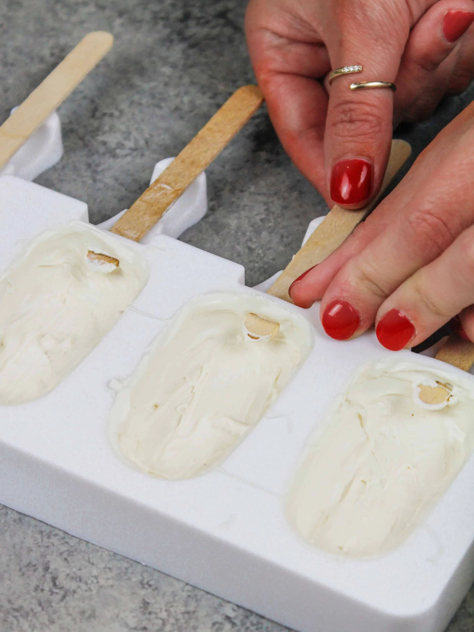 image of white chocolate and candy melts being painted into a silicone mold to make cakesicles, while inserting a popsicle stick to keep the opening in the mold open for later