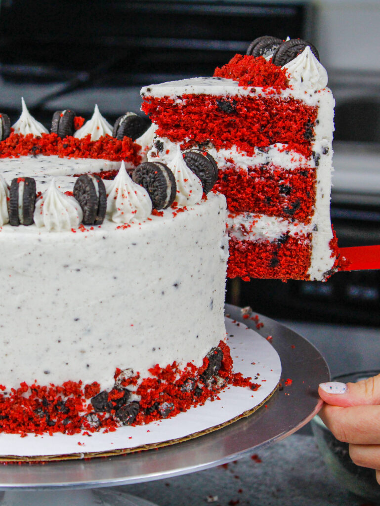 image of a red velvet oreo cake slice being pulled out of a cake that's frosted with oreo cream cheese frosting