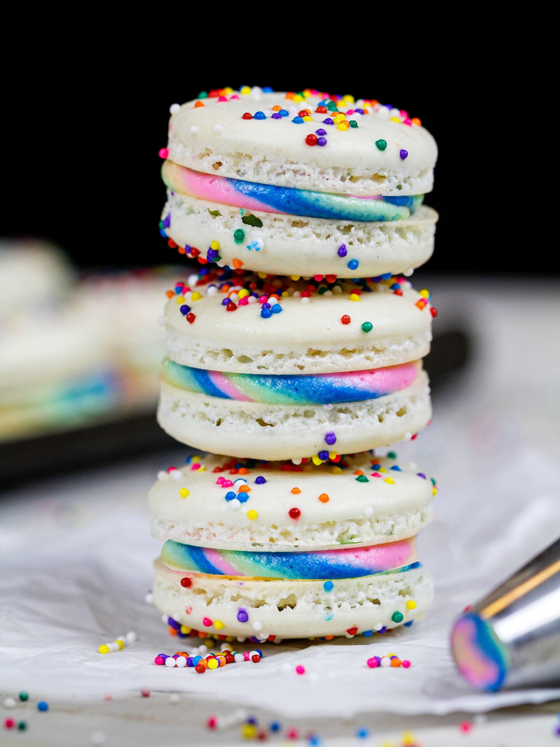 image of three rainbow macarons stacked on top of each other to show off their rainbow buttercream
