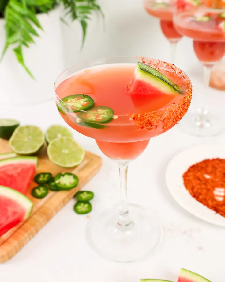 image of a jalapeno watermelon margarita in a margarita glass garnished with tajin and jalapeno slices