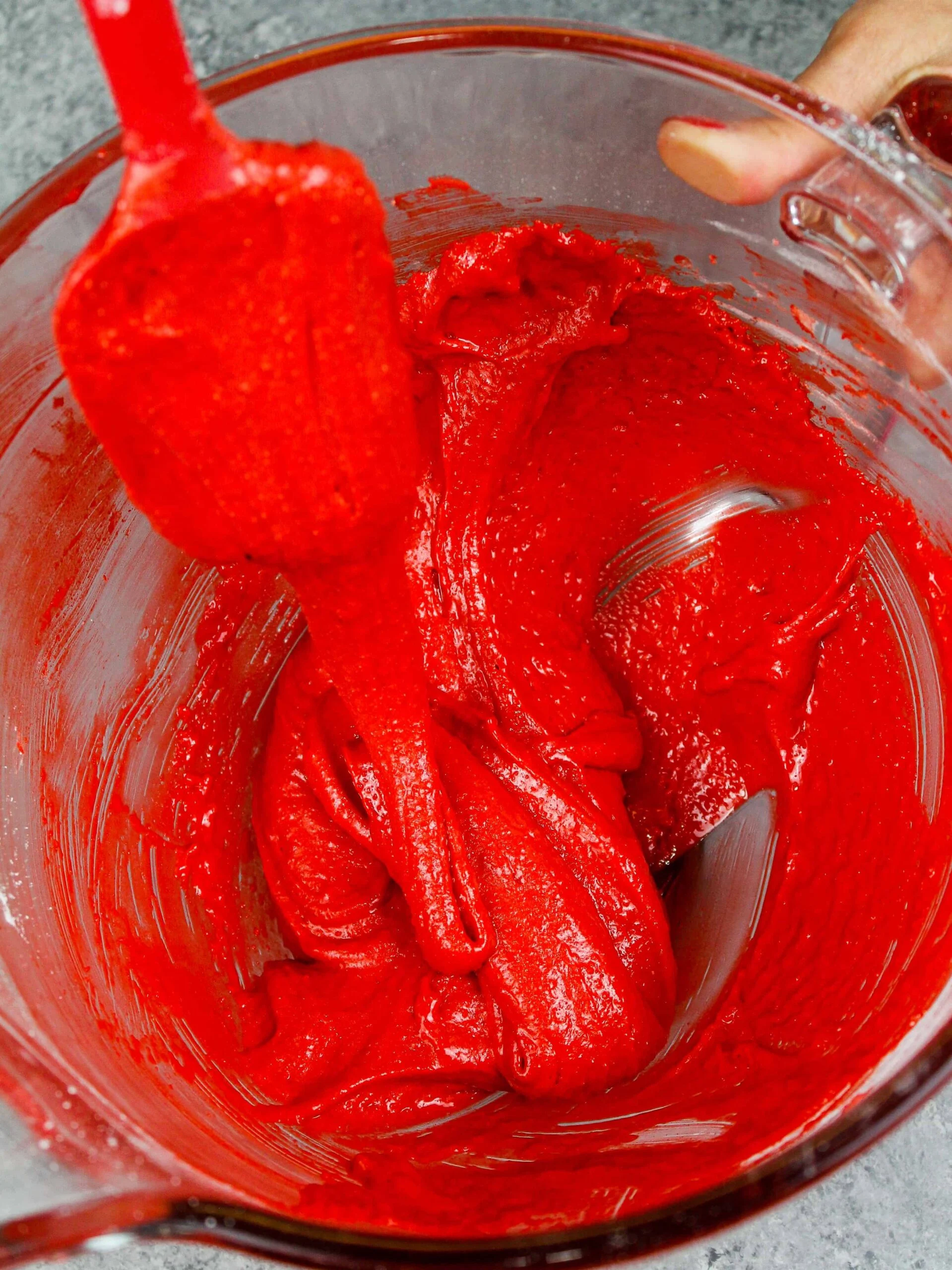 image of red velvet macaron batter that has been mixed to the perfect consistency so that it flows in thick ribbons off the spatula when lifted