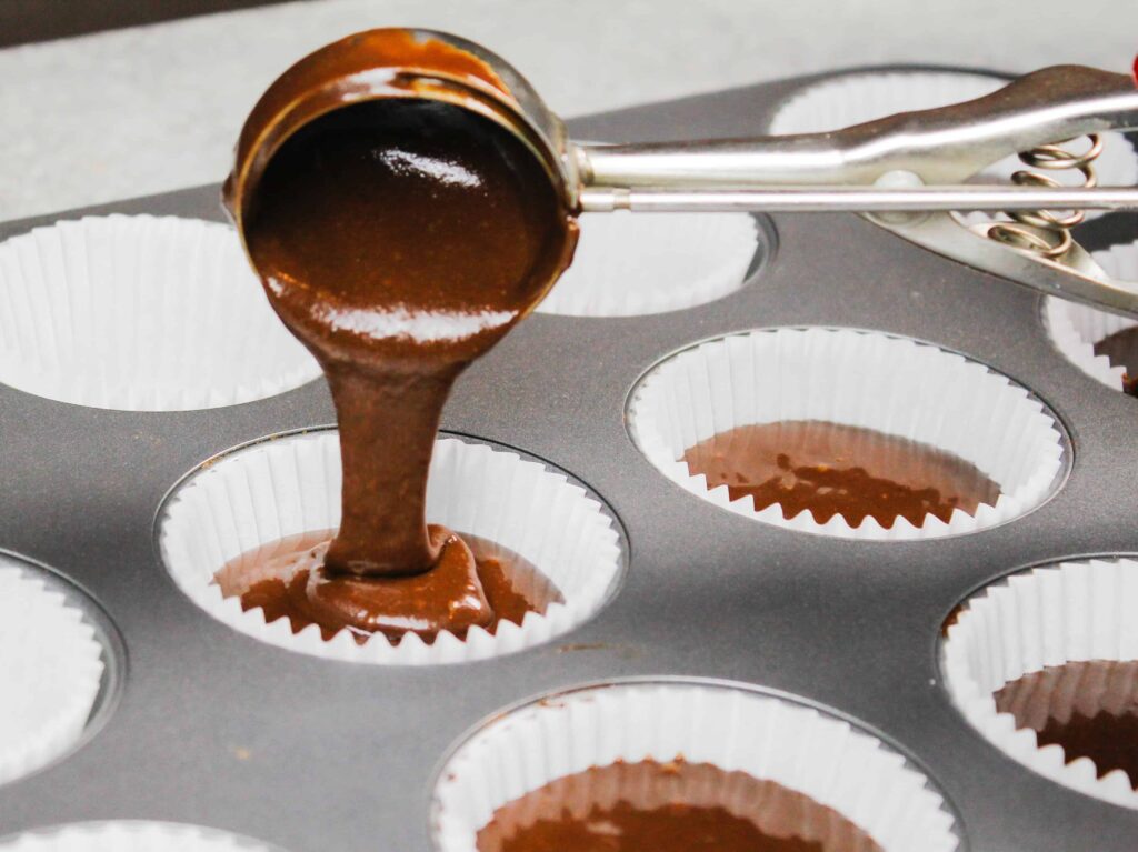 image of chocolate cupcake batter being scooped into a cupcake liner