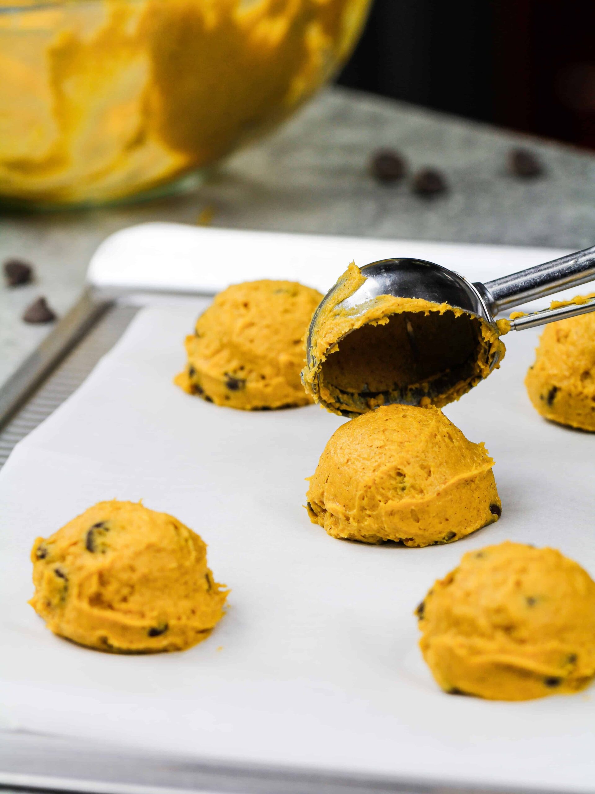 image of vegan chocolate chip pumpkin cookies being scooped onto a lined baking sheet with a cookie scoop