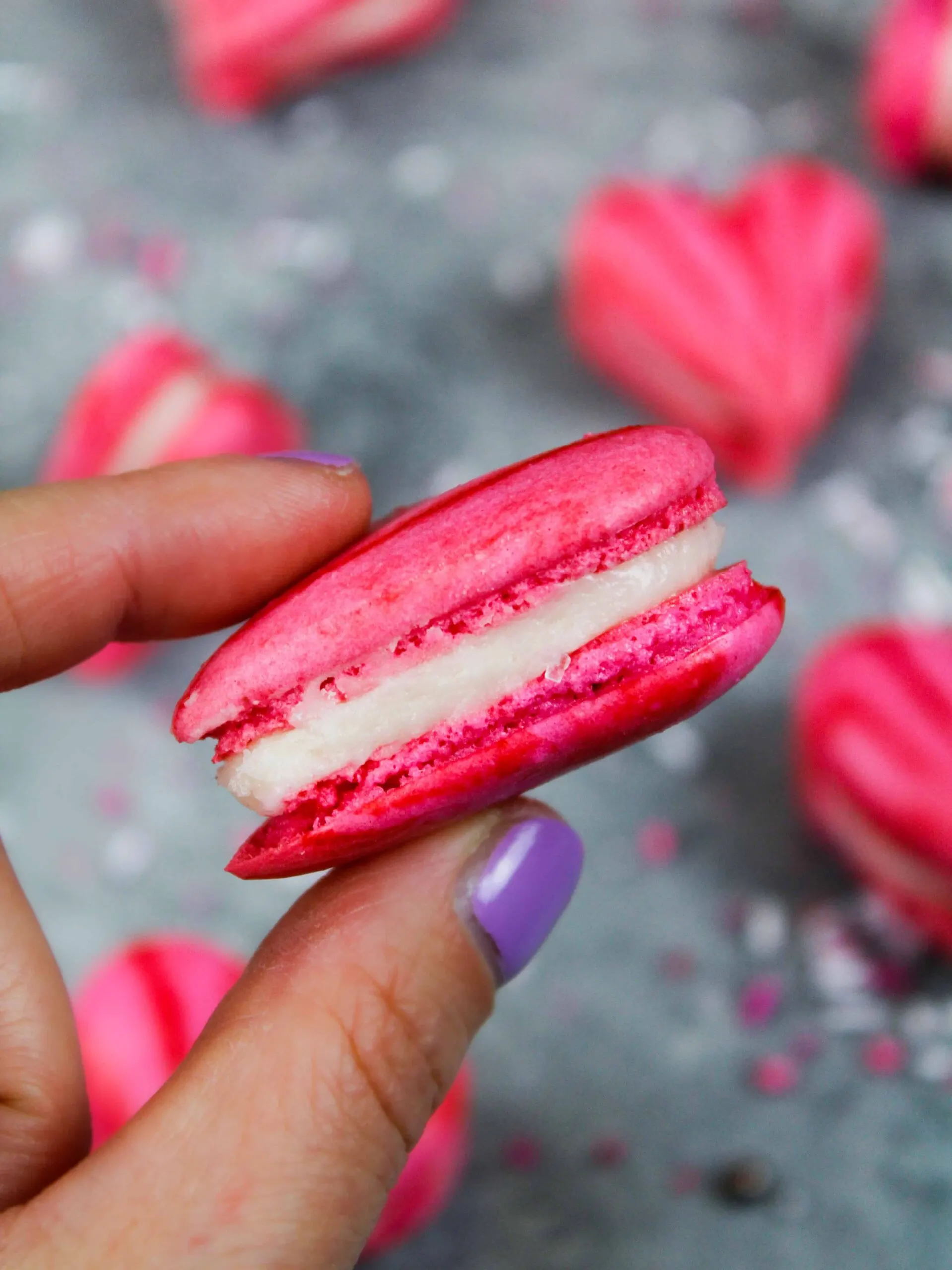 image of the side of a heart shaped macaron showing its buttercream filling and perfect feet