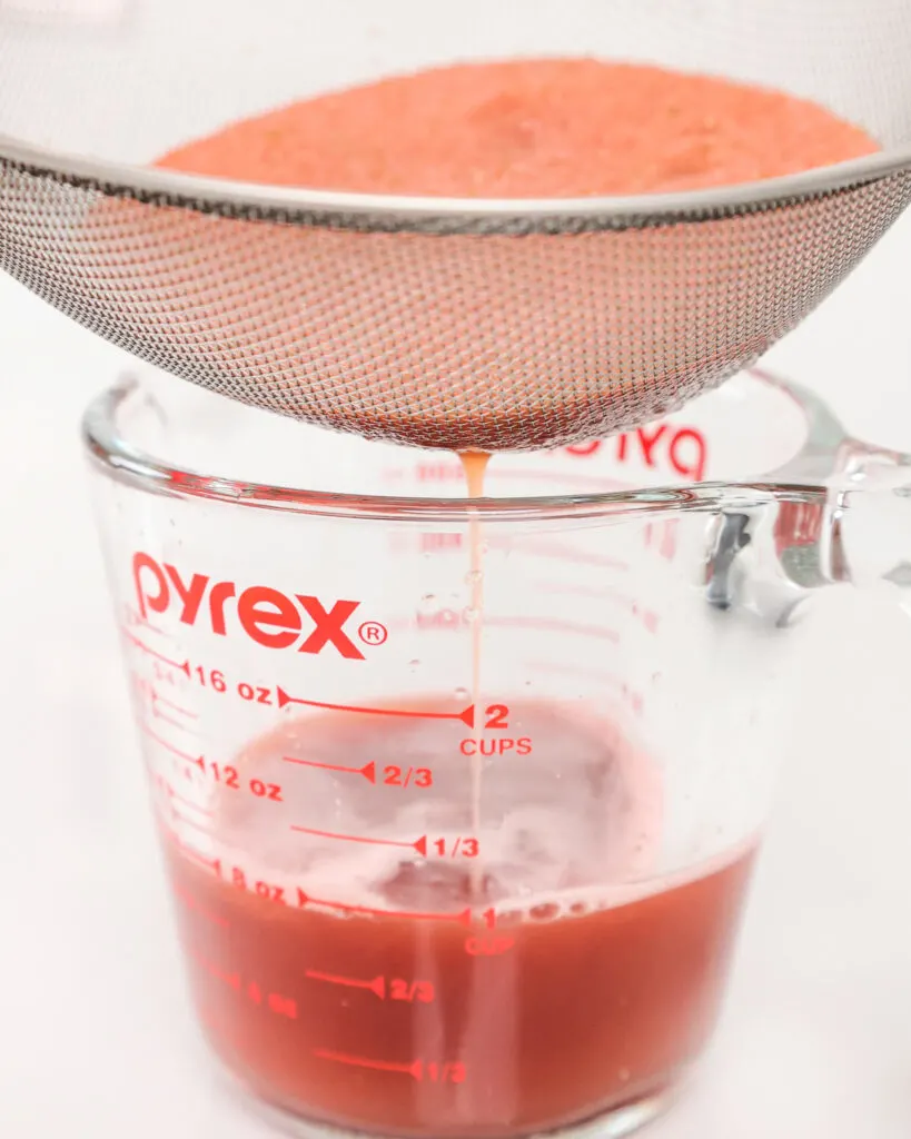 image of blended watermelon and jalapeno being poured through a strainer to make spicy watermelon juice