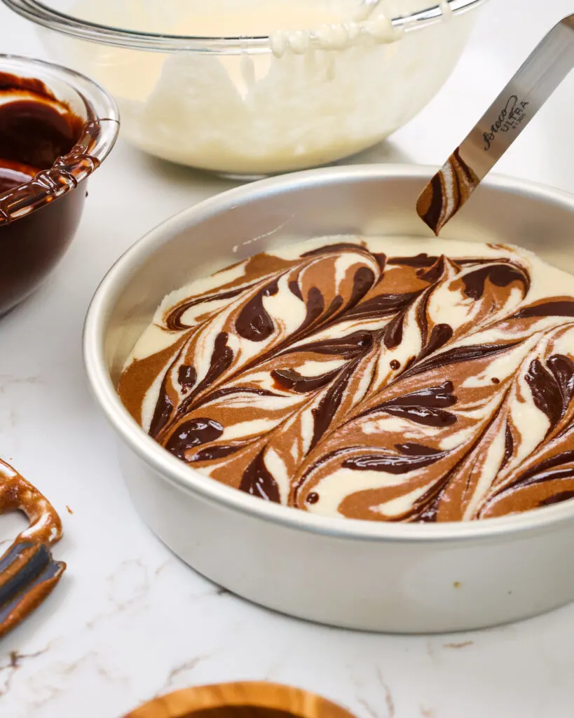 image of chocolate fudge being added into marble cake layers to make a fudge ripple swirl