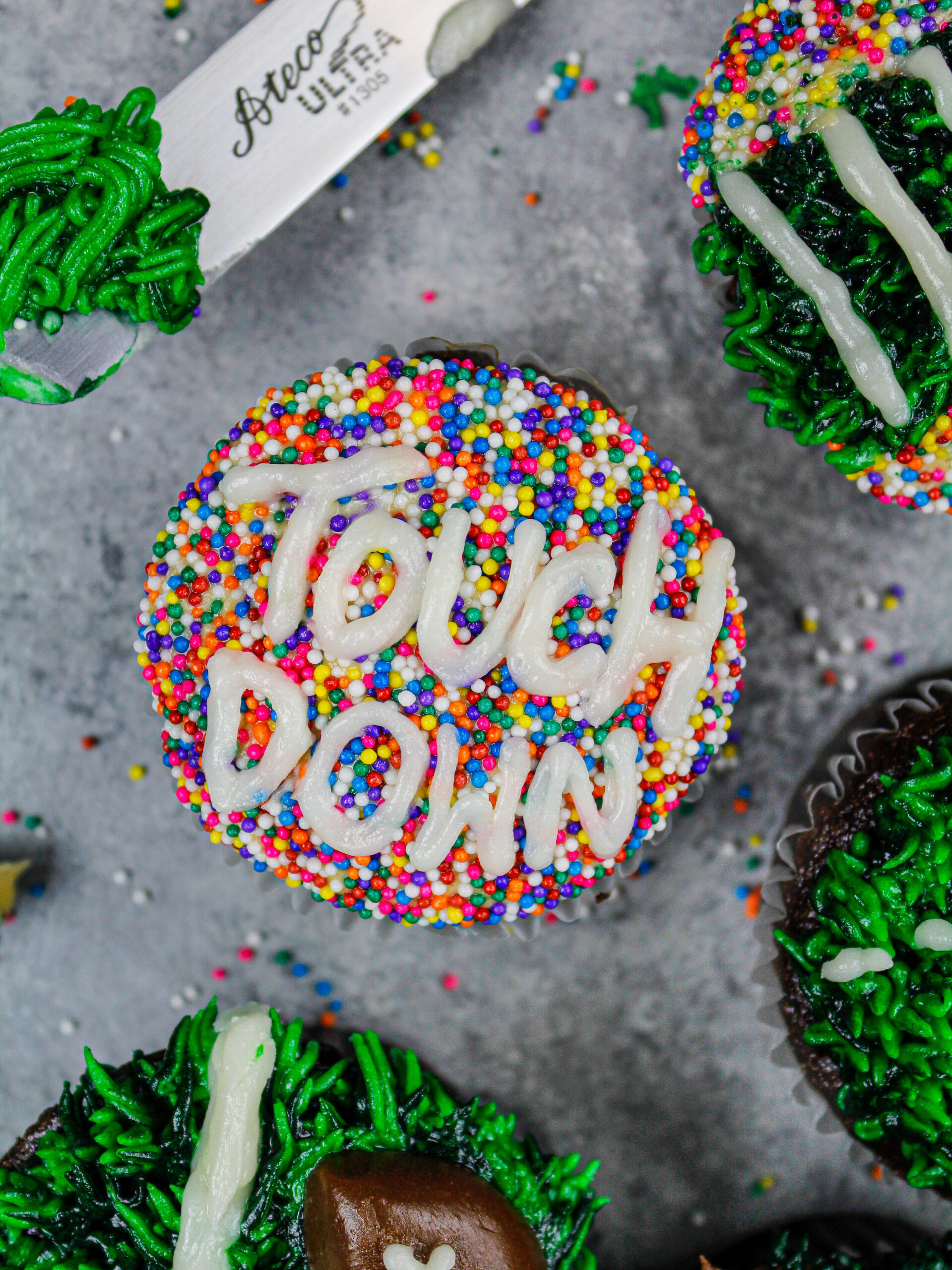 image of a football cupcake decorated with white buttercream and sprinkles to say touchdown