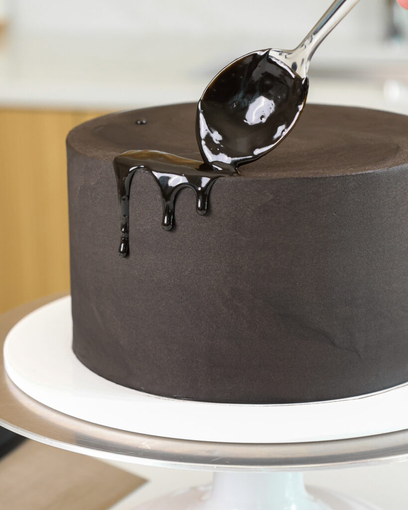 image of a black velvet cake being decorated with black drips that are added using a spoon