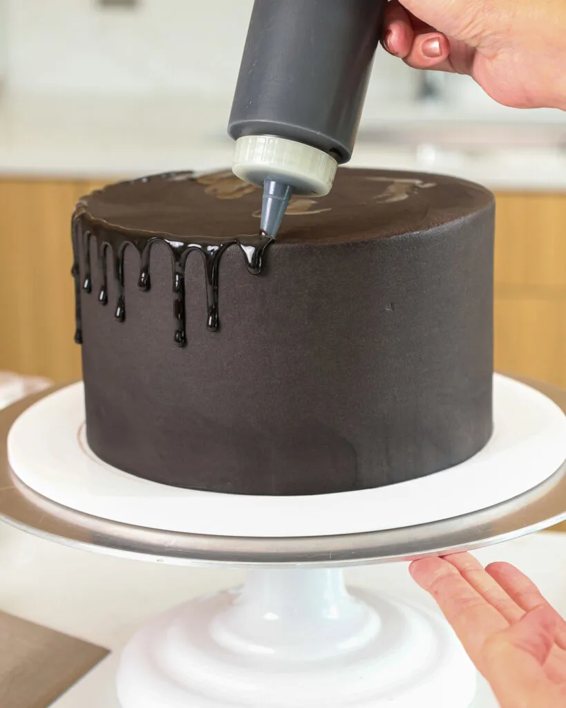 image of a black buttercream cake that's being decorated with black ganache drips using a plastic squirt bottle