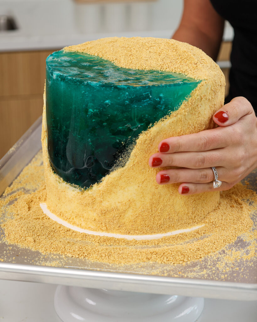 image of graham cracker crumbs being pressed into the side of a beach cake to look like sand