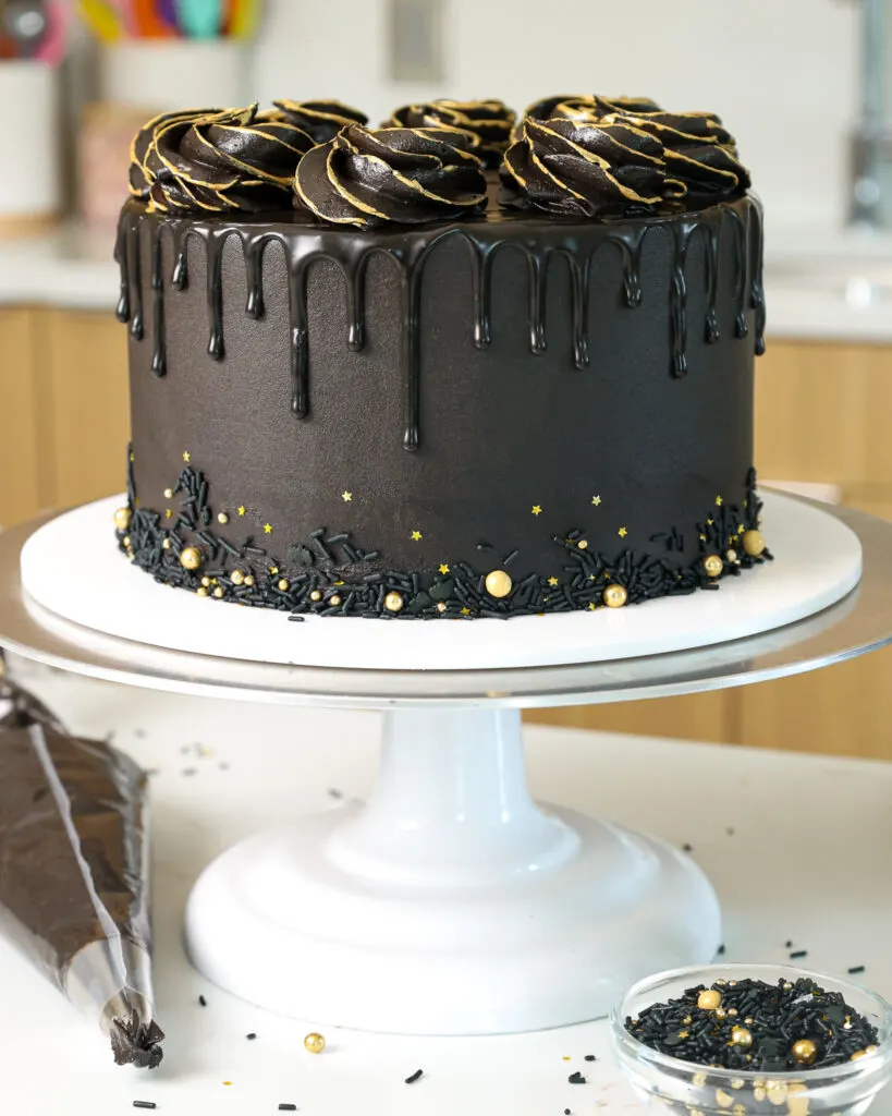 image of a black drip cake that's been decorated with gold sprinkles and edible gold paint