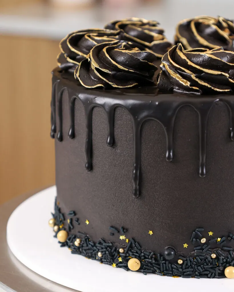 image of a black drip cake that's been decorated with gold sprinkles and edible gold paint